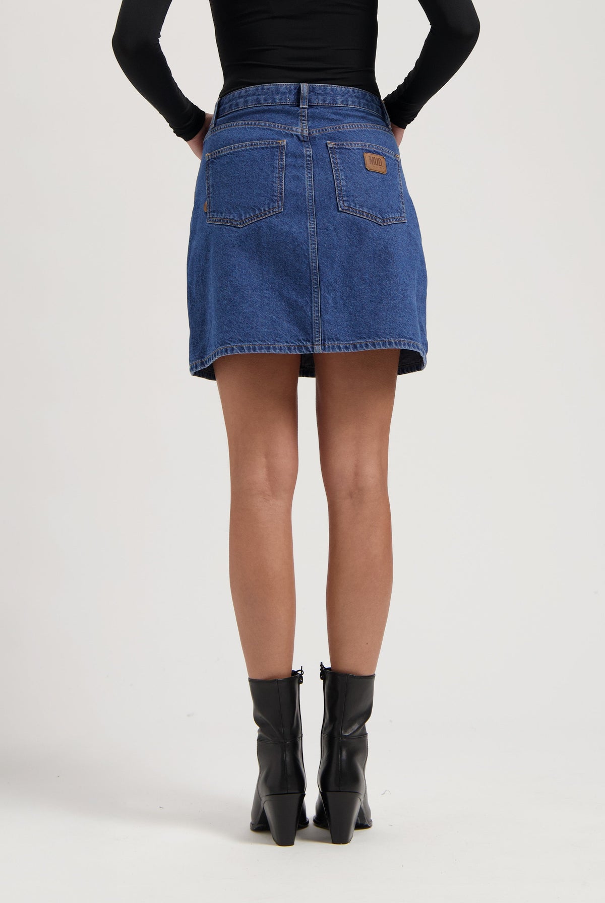 Denim A-line skirt in blue from MUD Jeans, paired with black leather ankle boots and a fitted long-sleeve black top.