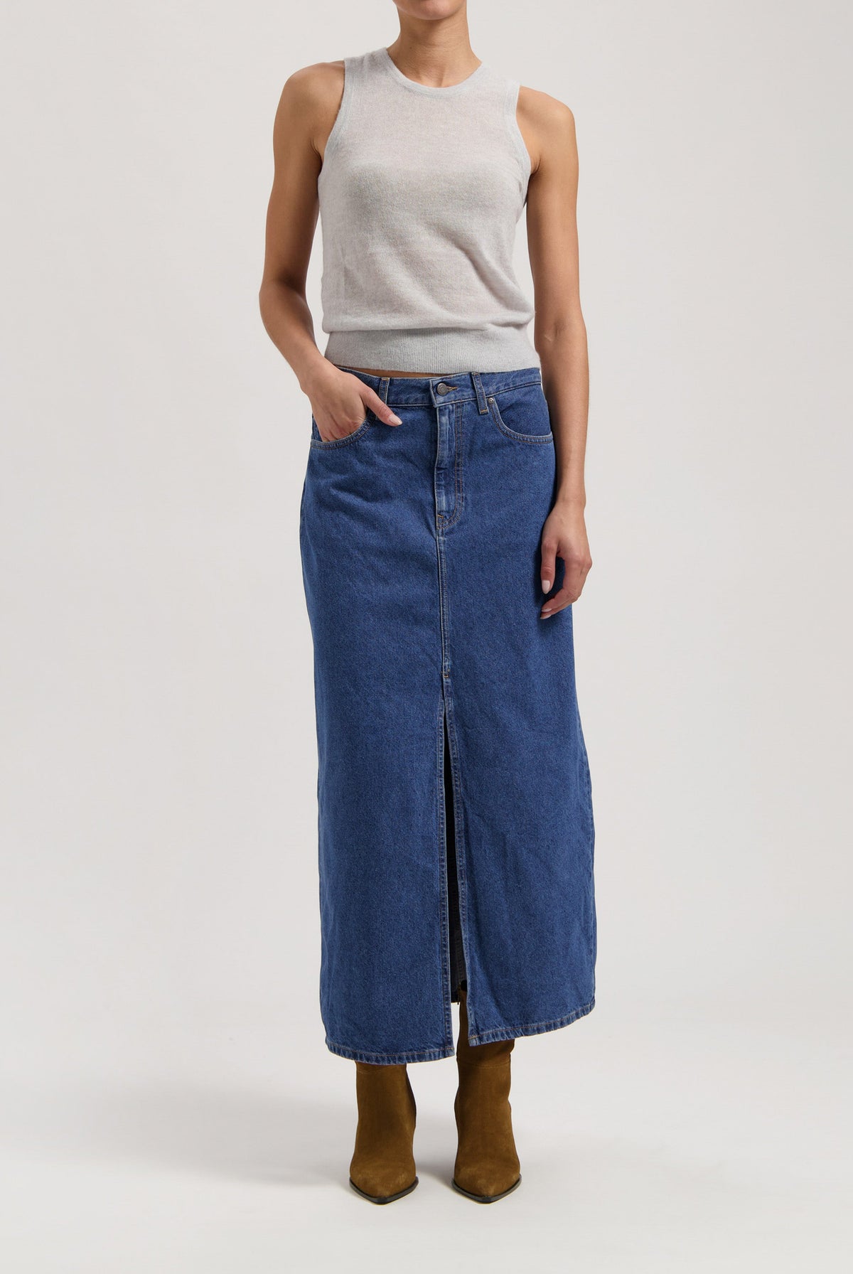 Long blue denim skirt with front slit, paired with a sleeveless gray top and brown pointy boots, showcasing casual chic style.