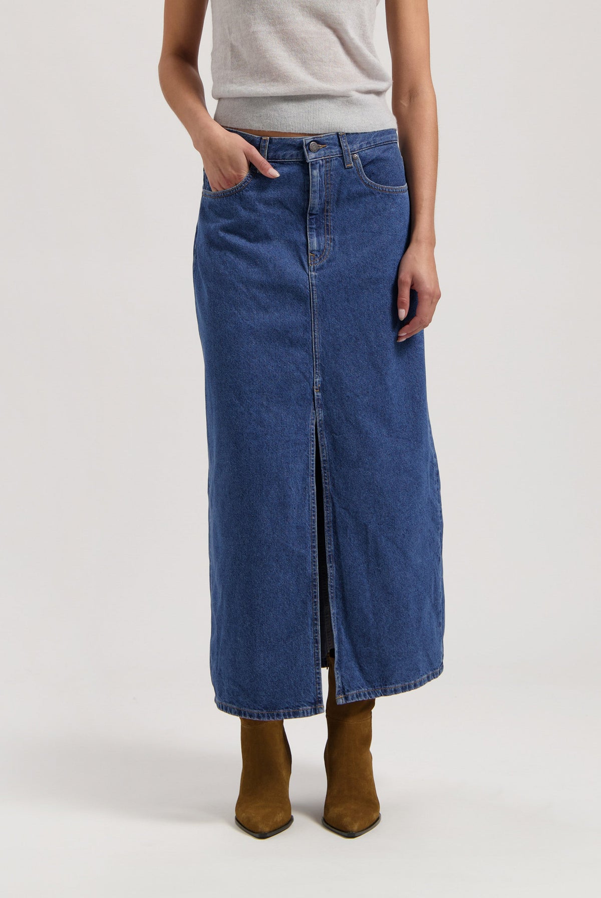 Woman wearing a long denim skirt with front slit, paired with a sleeveless gray top and brown suede ankle boots.