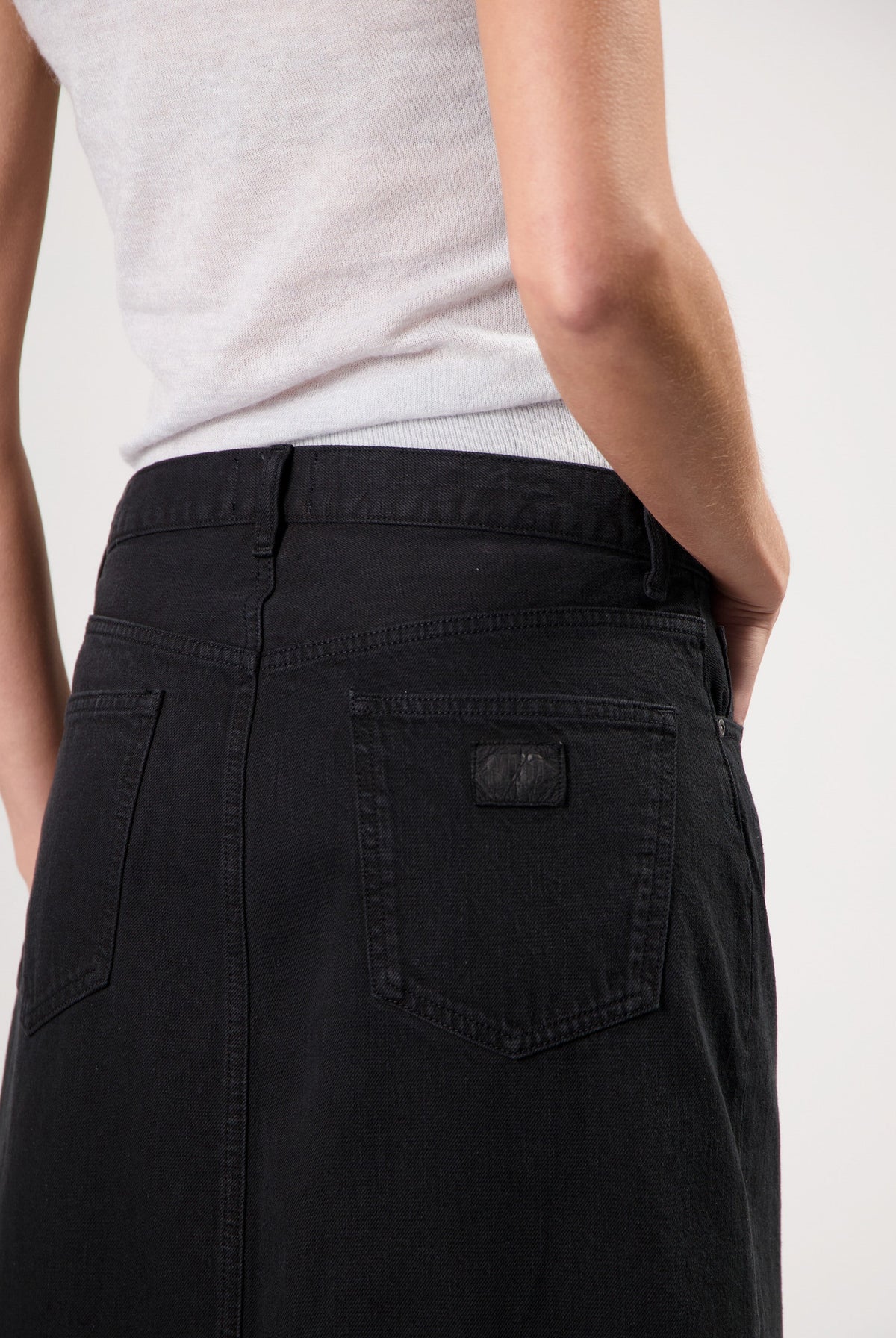 A close-up of a person wearing a fitted black denim skirt paired with a light gray sleeveless top, showcasing minimalist style.