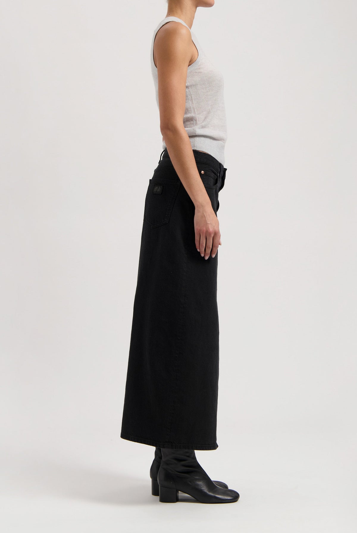 Black high-waisted, full-length denim skirt paired with a light gray sleeveless top and black ankle boots.