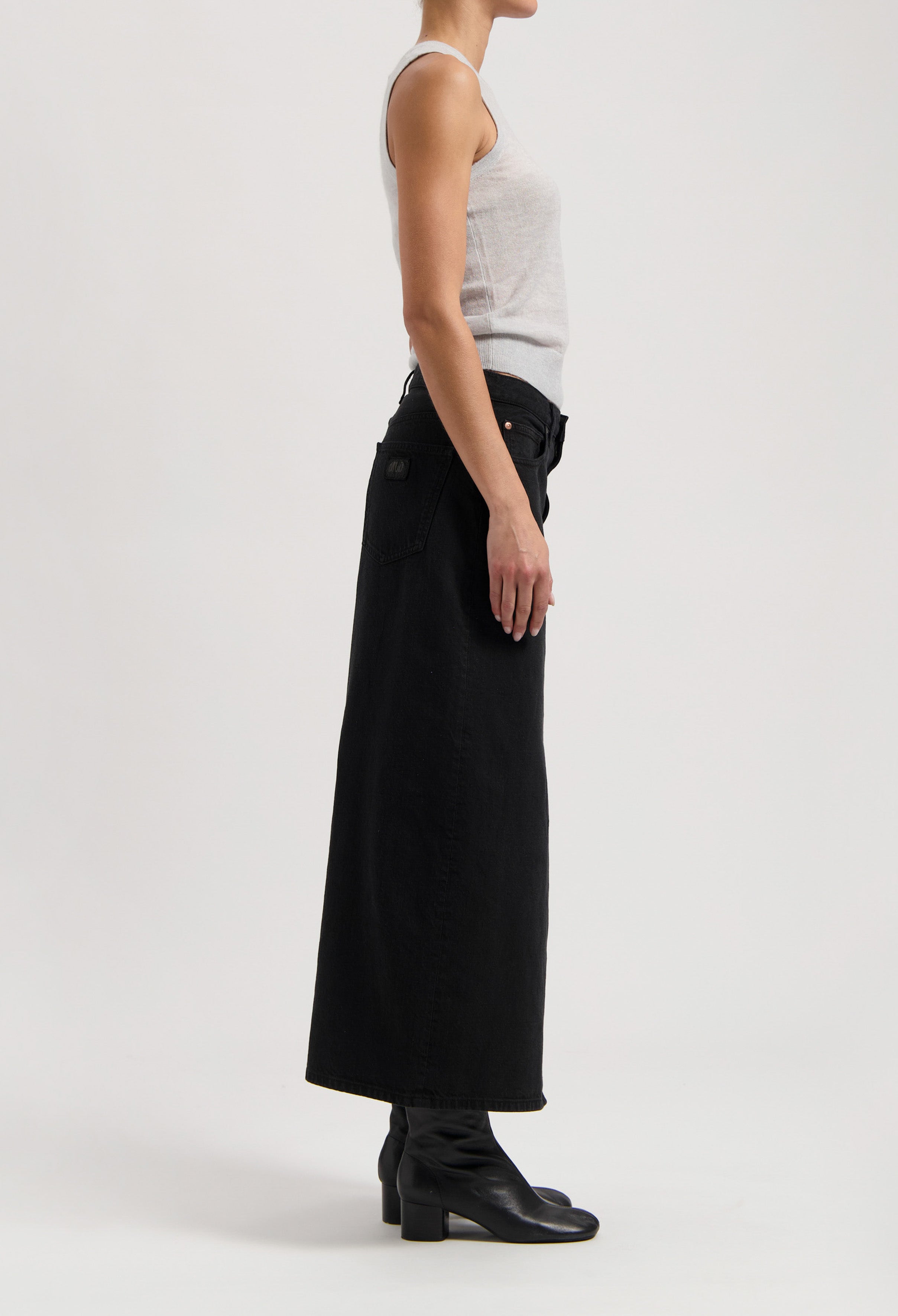 Black high-waisted, full-length denim skirt paired with a light gray sleeveless top and black ankle boots.