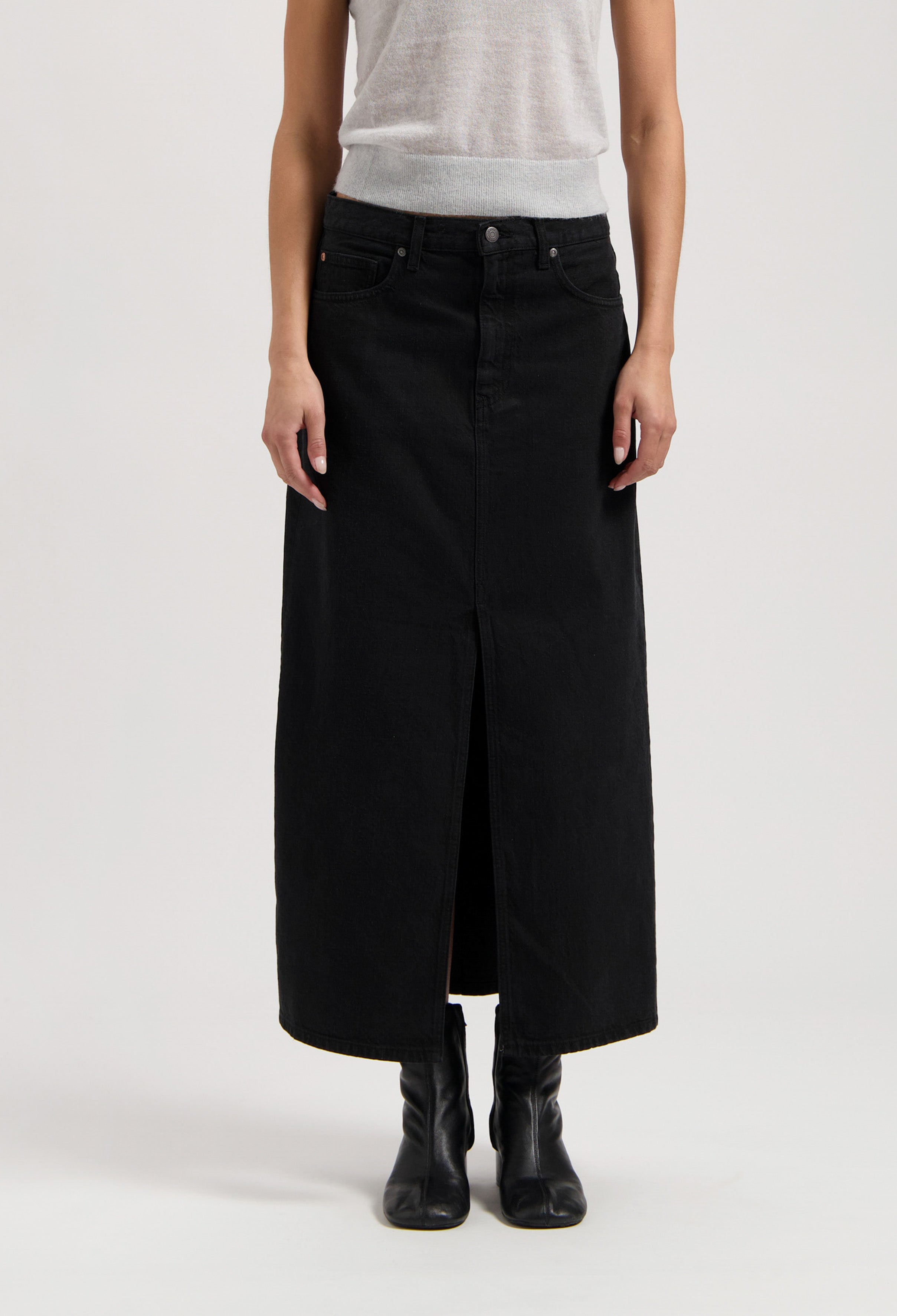 Black denim long skirt with a front slit, paired with a sleeveless light gray top and black ankle boots.