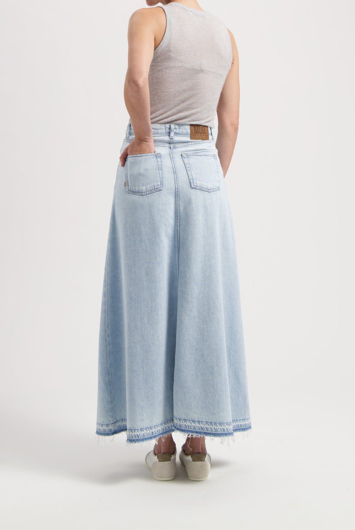 Light blue, high-waisted denim maxi skirt with raw hem, worn with a sleeveless gray top, showcasing sustainable MUD Jeans.