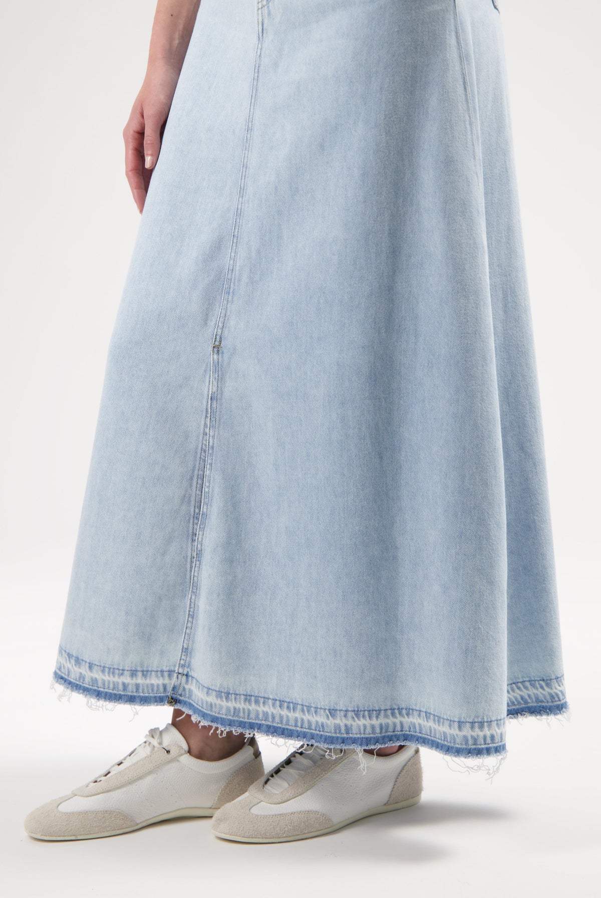 Light blue denim maxi skirt with frayed hem, paired with white and beige canvas sneakers in a minimalist style.