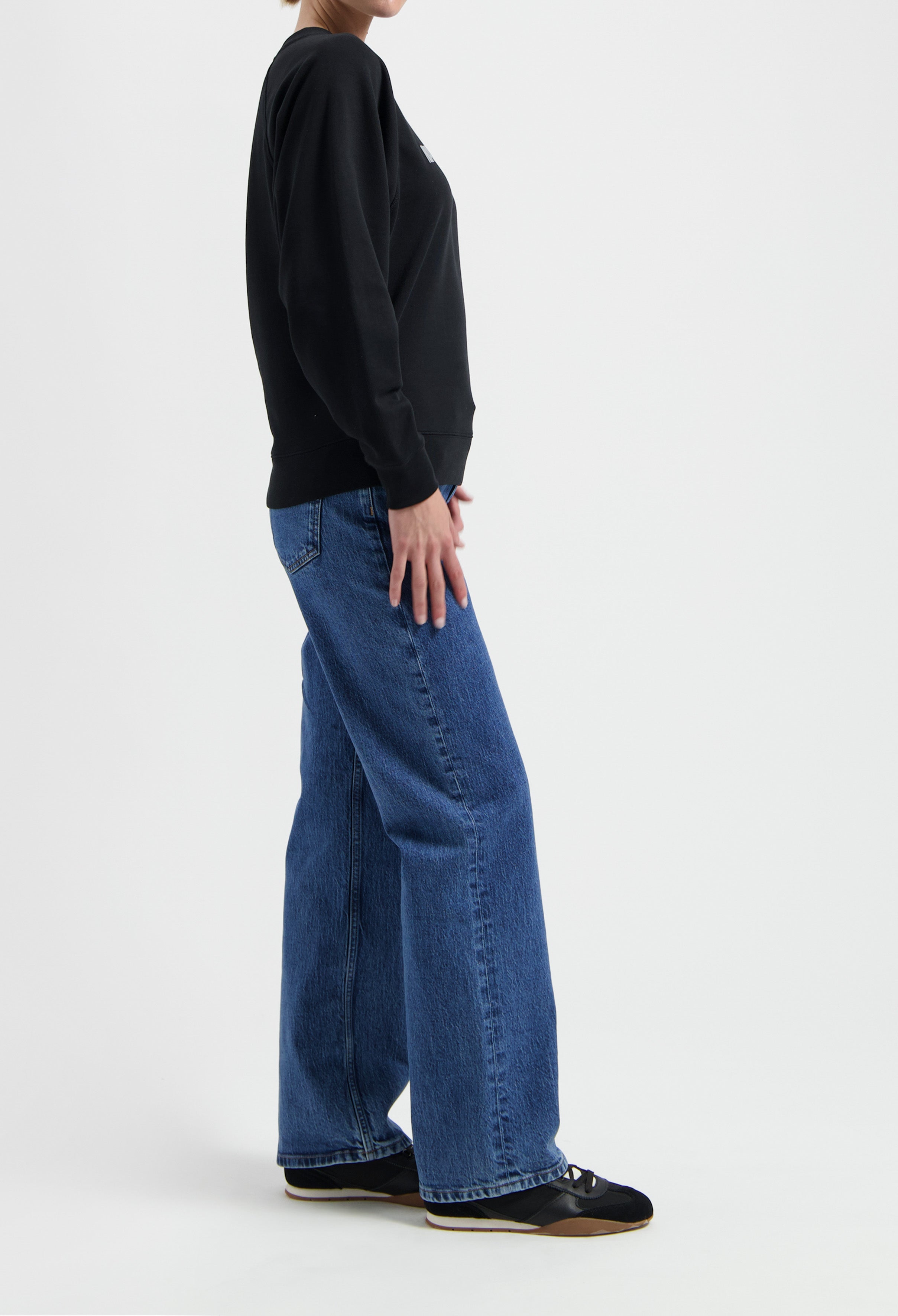 Casual outfit with wide-leg blue denim jeans and a black sweatshirt, paired with black sneakers on a neutral background.