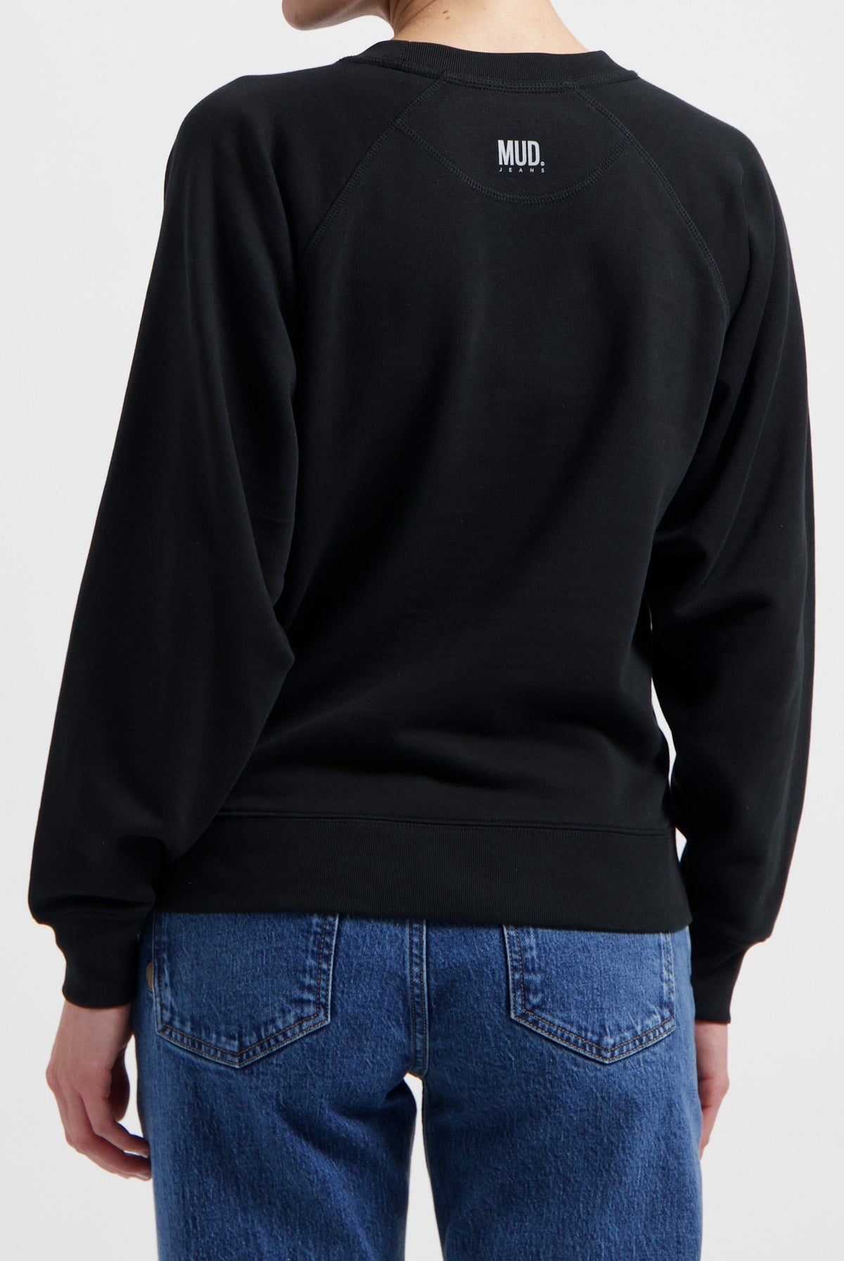 Black MUD Jeans sweatshirt with simple logo, paired with blue denim jeans, showcasing casual and comfortable style.
