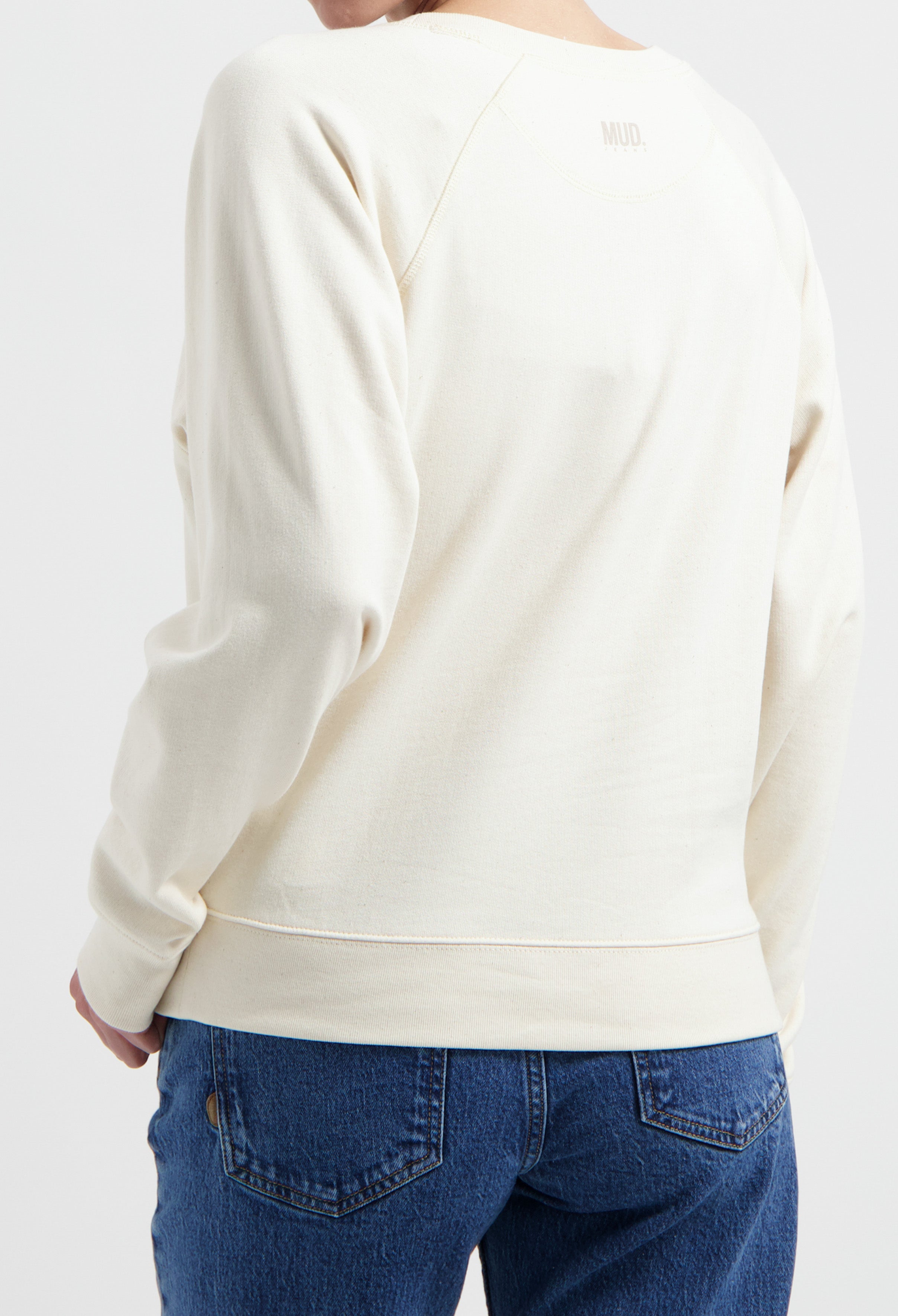 Off-white MUD sweatshirt paired with blue denim jeans, showcasing a sustainable fashion choice with relaxed fit and style.