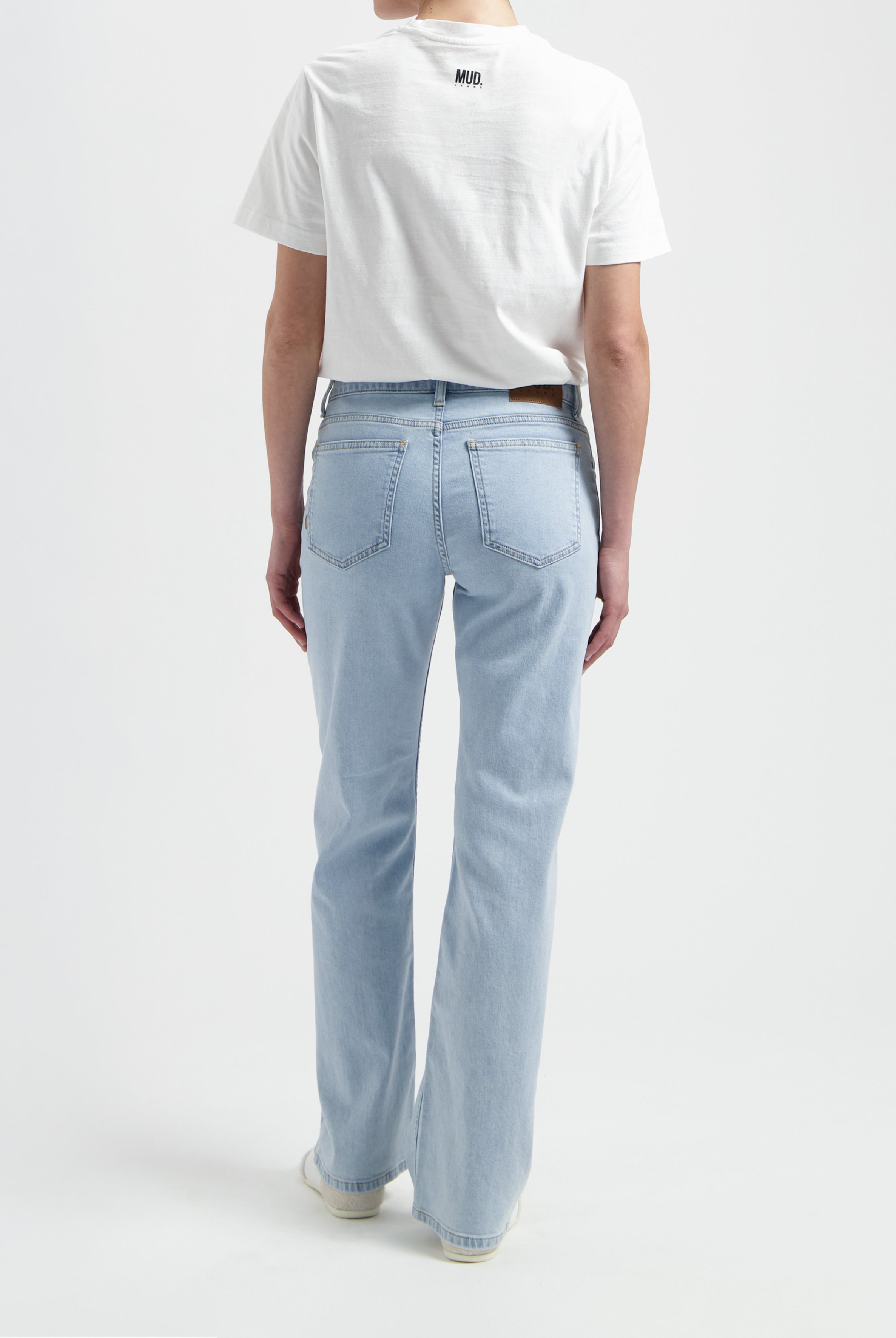 Model wearing light blue MUD Jeans made from organic cotton, paired with a white short-sleeve top, viewed from the back.
