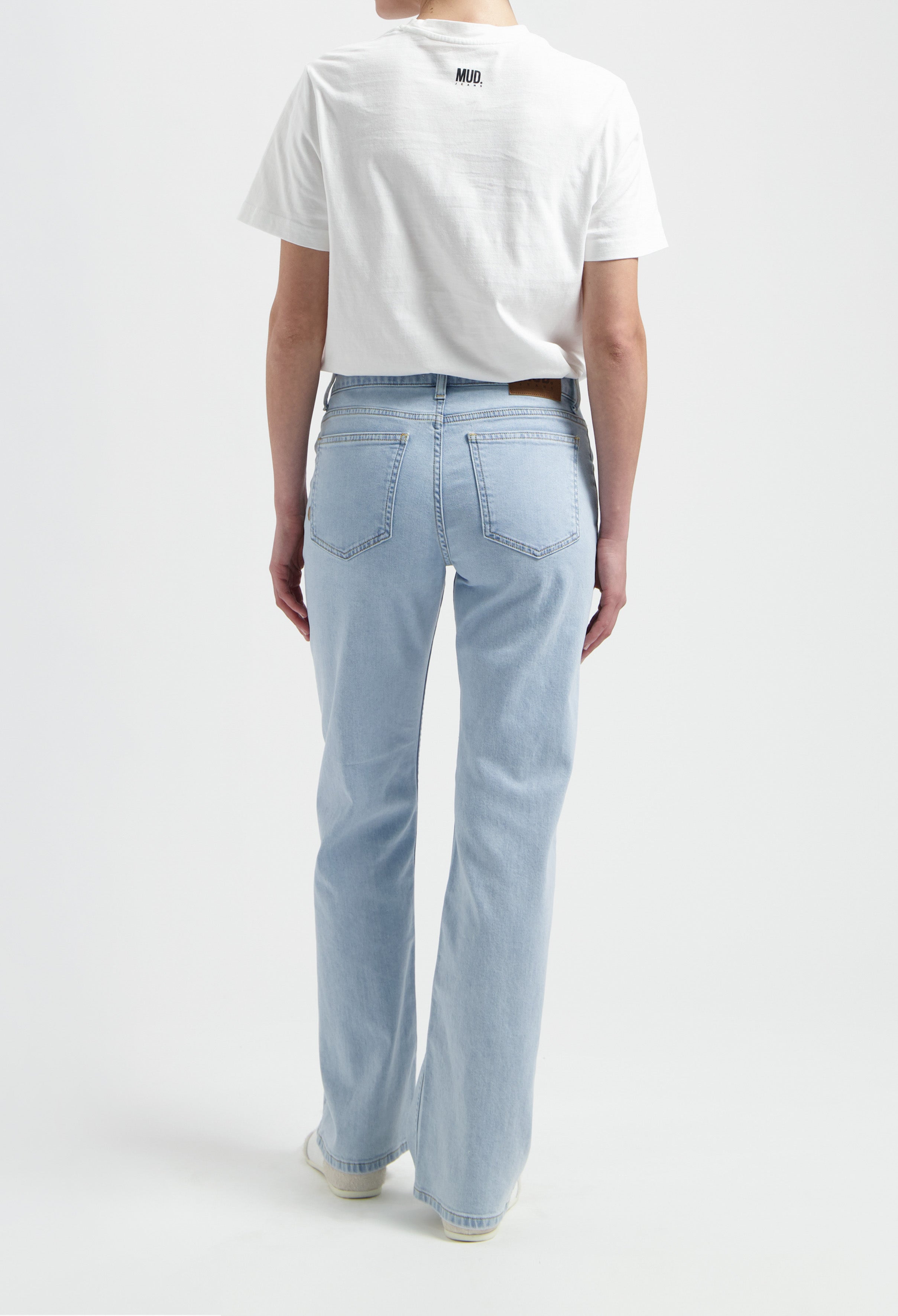 Model wearing light blue MUD Jeans made from organic cotton, paired with a white short-sleeve top, viewed from the back.