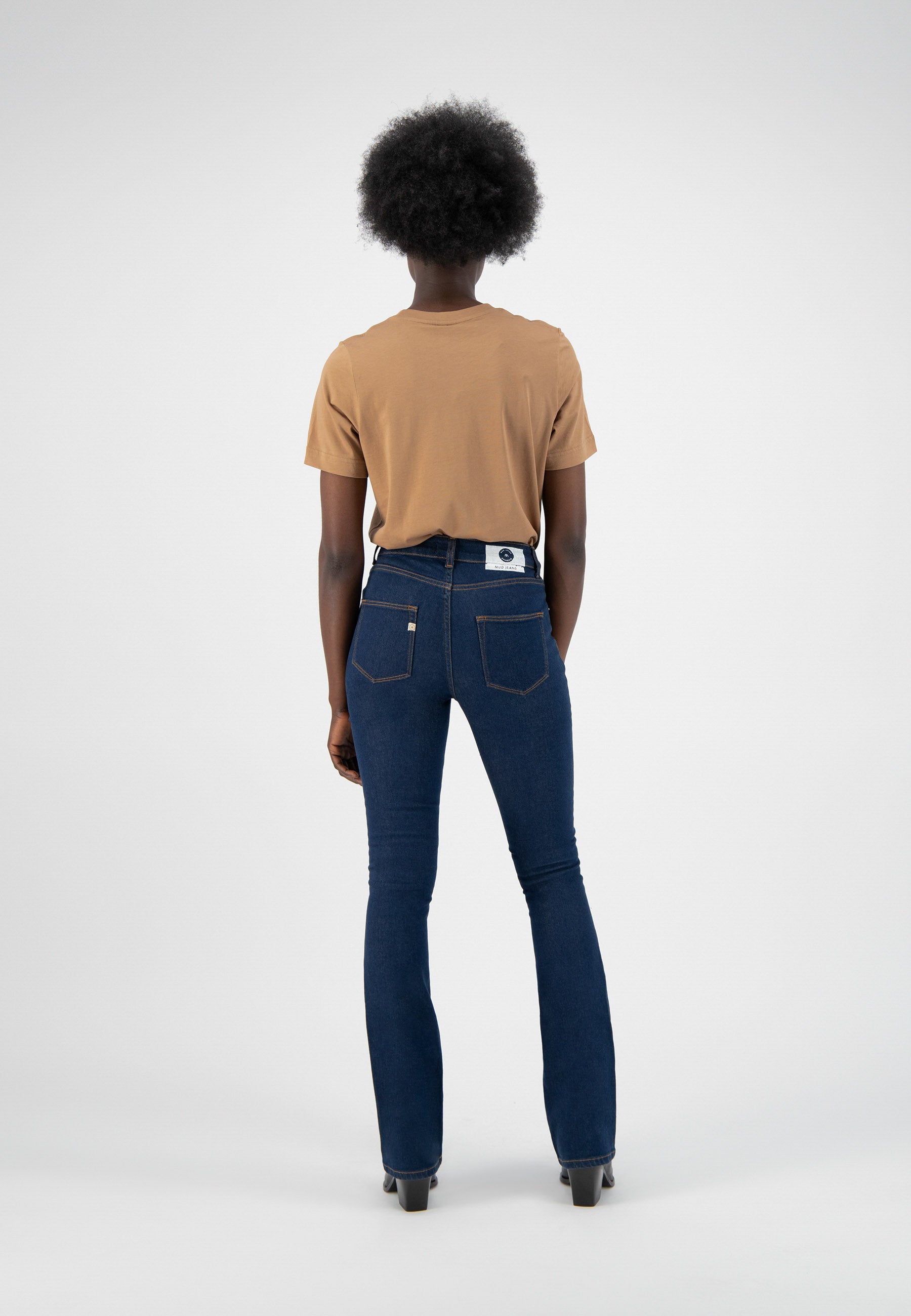 Model wearing dark blue denim jeans with a fitted high waist, paired with a tan short-sleeve top, displaying a casual style.