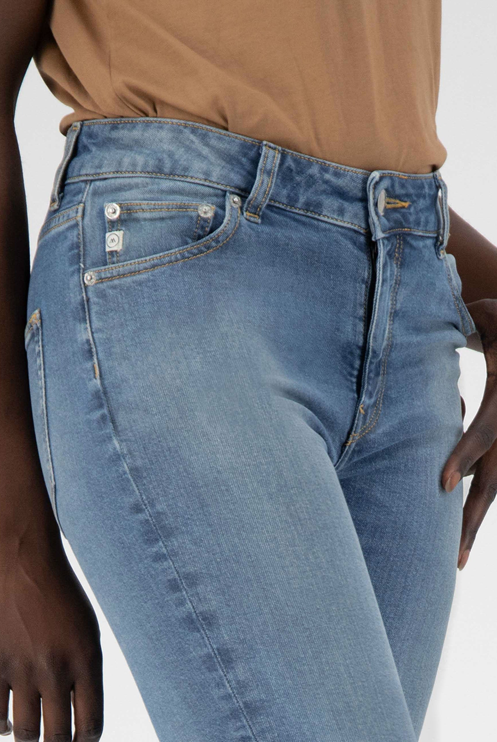 Close-up of light blue denim jeans with a high-rise waist and slim fit, paired with a tan top showing casual style.