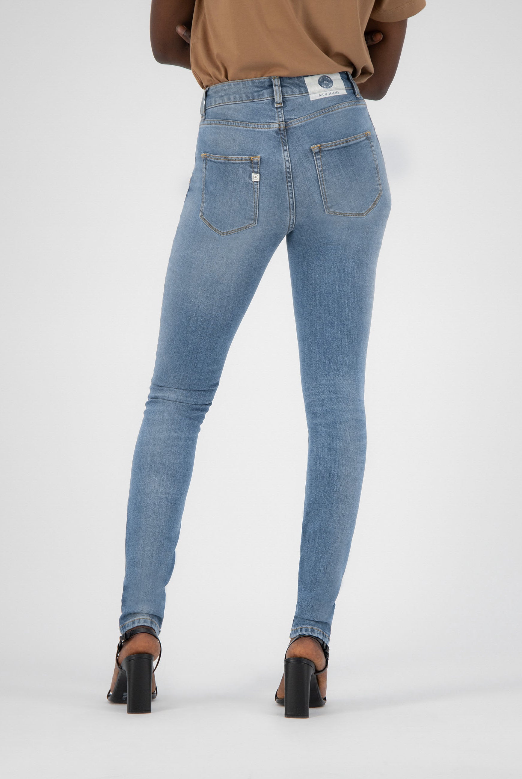 High-waisted light blue skinny jeans from MUD Jeans, showcasing back pockets and paired with black heels.
