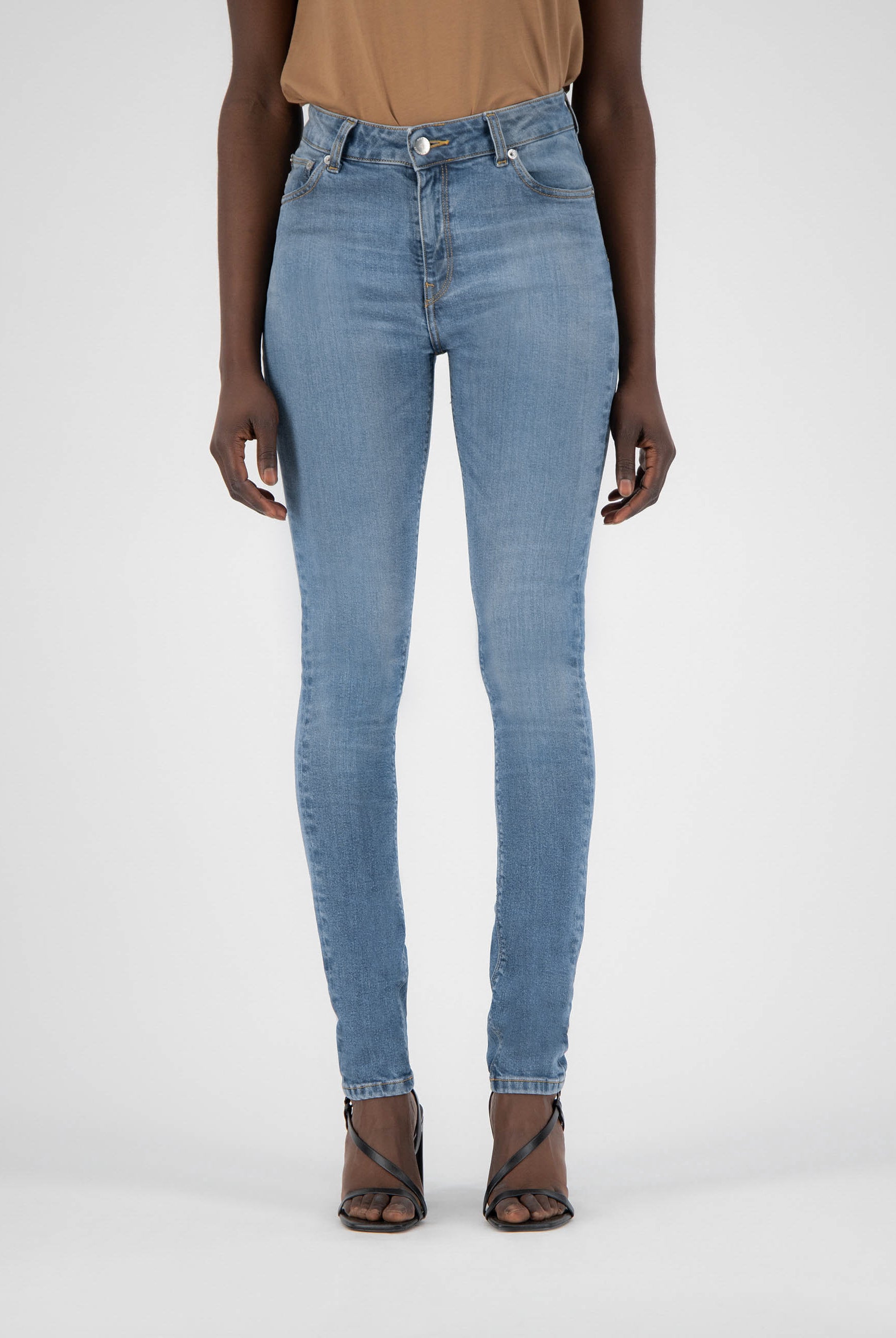 Light blue high-waisted skinny jeans worn with a beige sleeveless top and black strappy heels on a plain background.