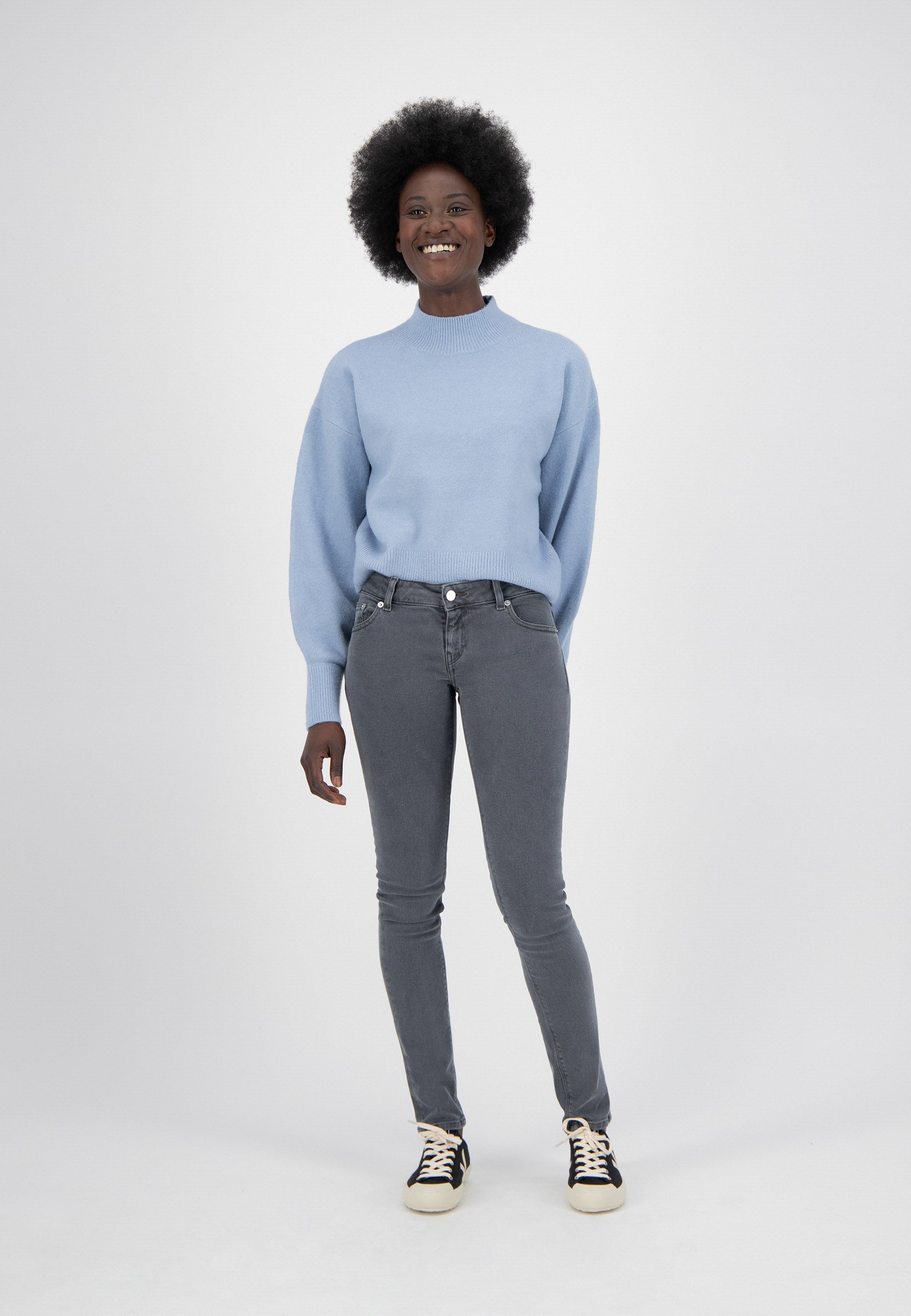 Person wearing a light blue sweater with puffed sleeves and fitted gray jeans, paired with black and white sneakers.