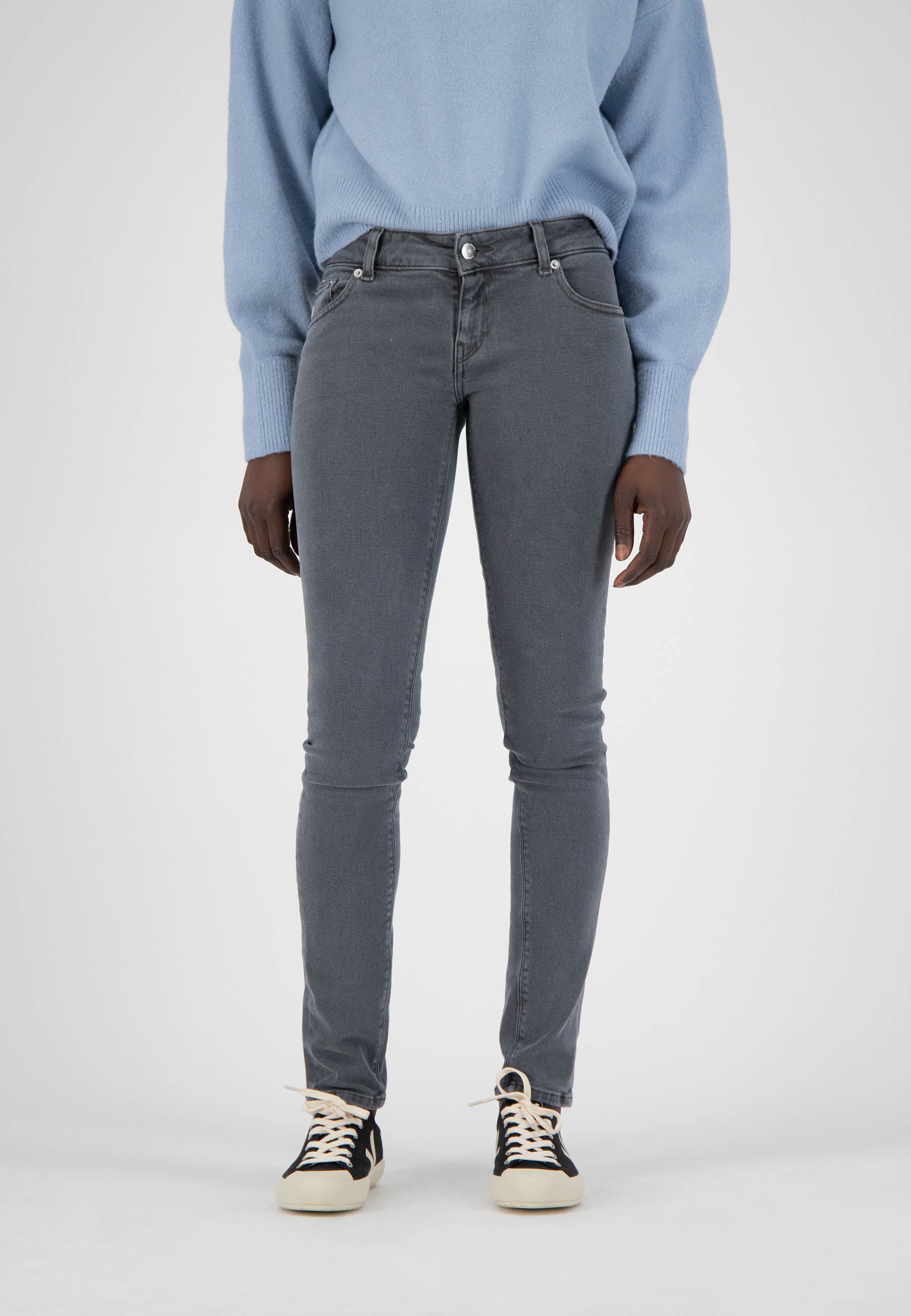 A model wearing slim-fit gray jeans paired with black and white sneakers and a cozy light blue sweater.