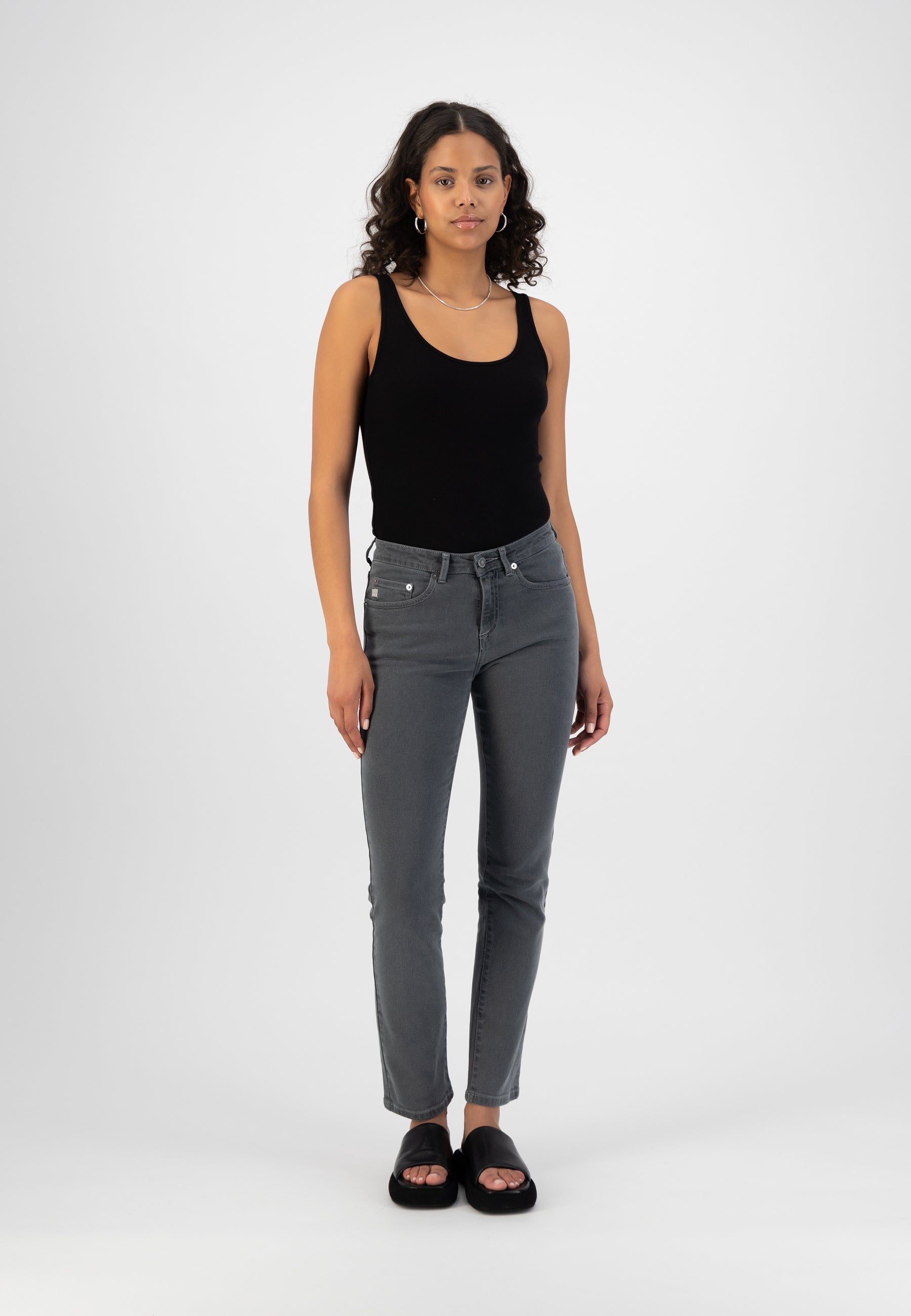 Model in gray slim-fit jeans with a black sleeveless top and black slip-on sandals, showcasing casual minimalist style.