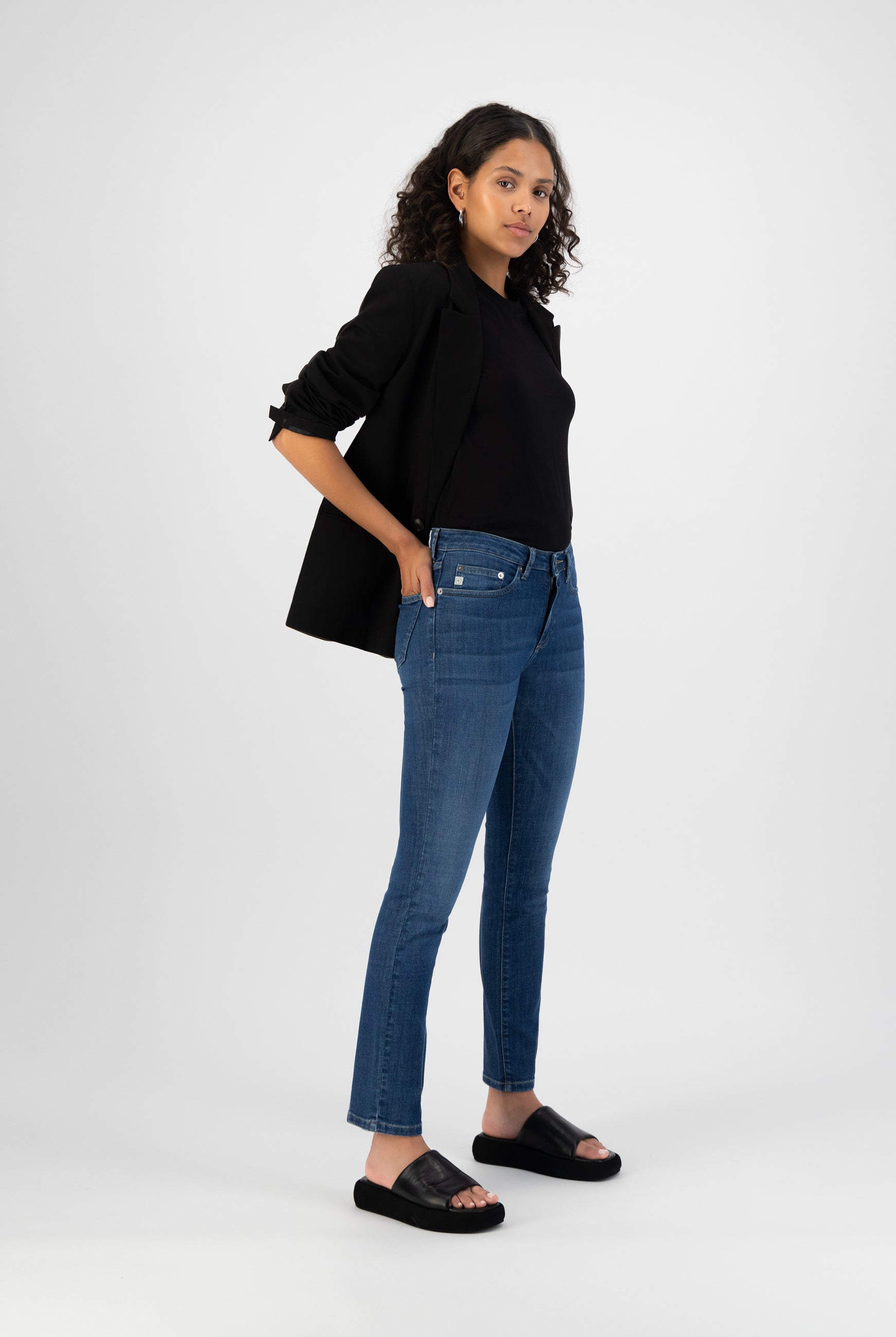 Modern casual outfit with dark blazer, black top, slim-fit blue jeans, and black slide sandals, showcasing contemporary style.