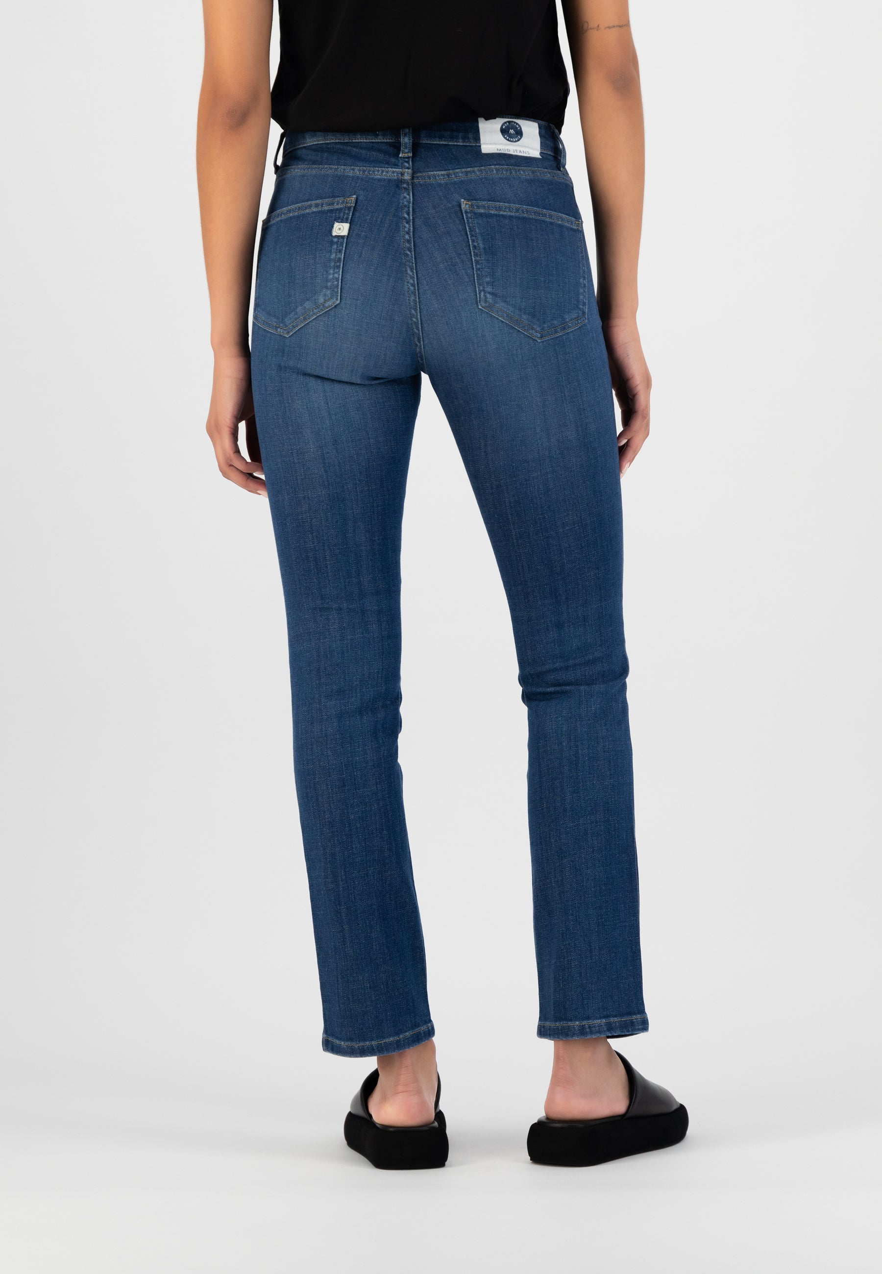 Model wearing eco-friendly dark blue straight-leg denim jeans, back view, paired with a black sleeveless top.