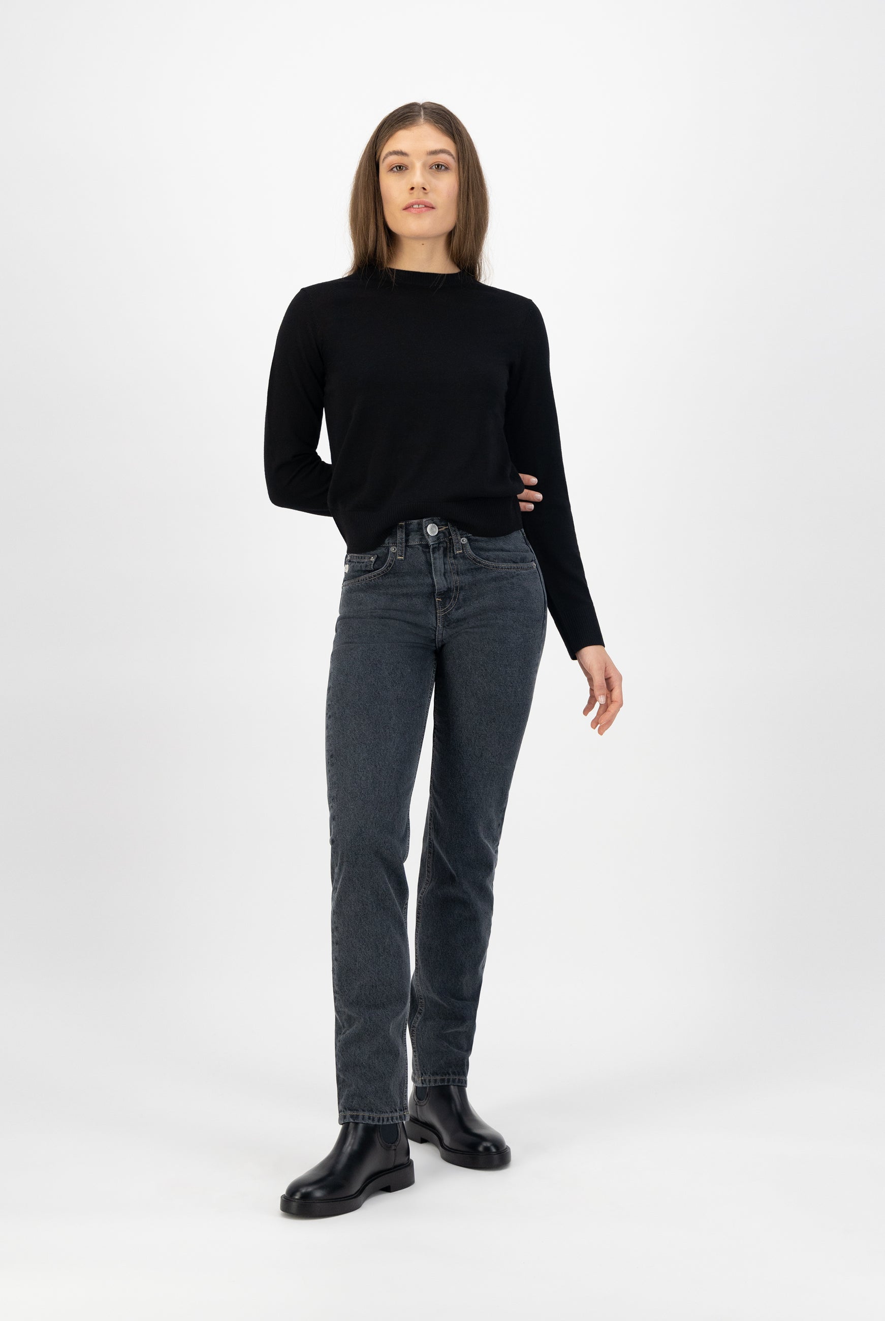A woman wearing dark wash jeans paired with a black long-sleeve top and black leather ankle boots in a minimalist style.
