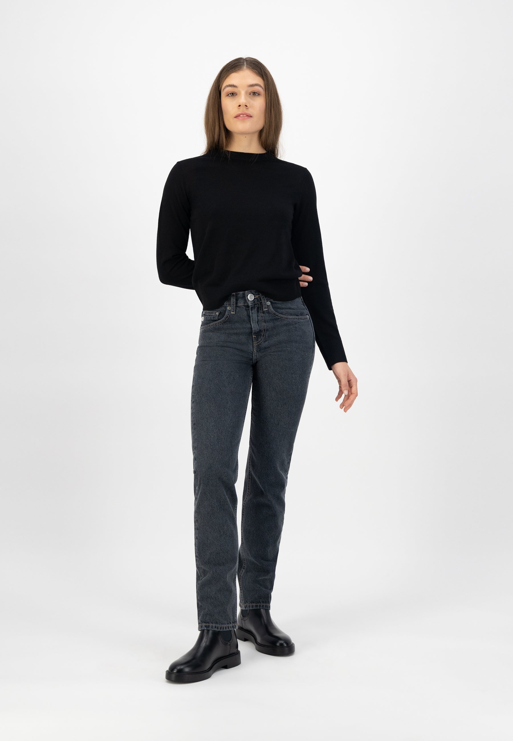 A woman wearing dark wash jeans paired with a black long-sleeve top and black leather ankle boots in a minimalist style.