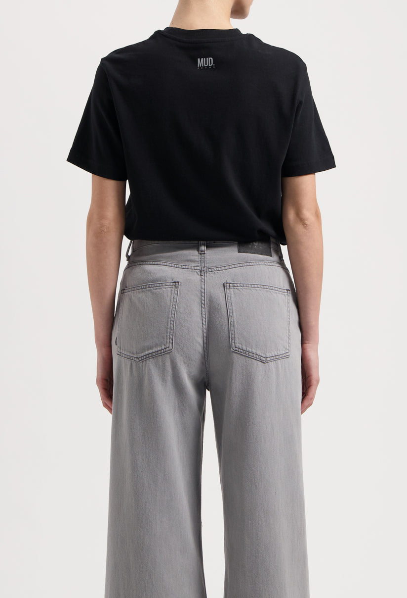 Sustainable MUD Jeans in dark brown, crafted from organic cotton, worn with a white t-shirt and white sneakers.