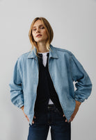 A casual light blue denim jacket worn over a navy shirt and white top, paired with dark blue jeans, perfect for a relaxed style.