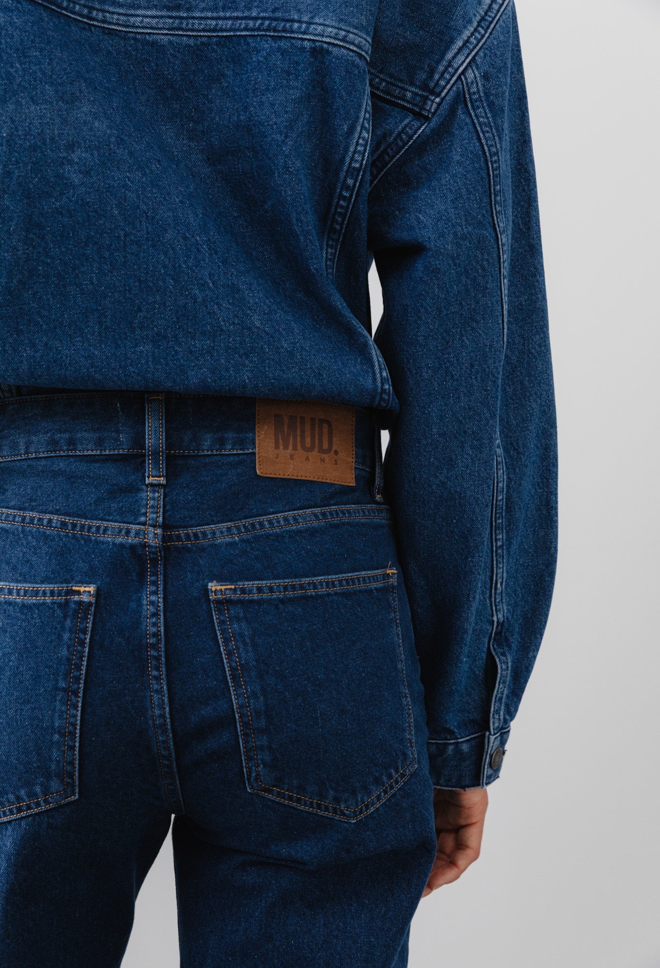 Back view of recycled dark blue denim jacket and jeans set, featuring MUD Jeans logo on leather patch above pocket.