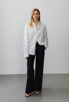Oversized white cotton button-up shirt paired with black wide-leg pants on gray concrete floor background.