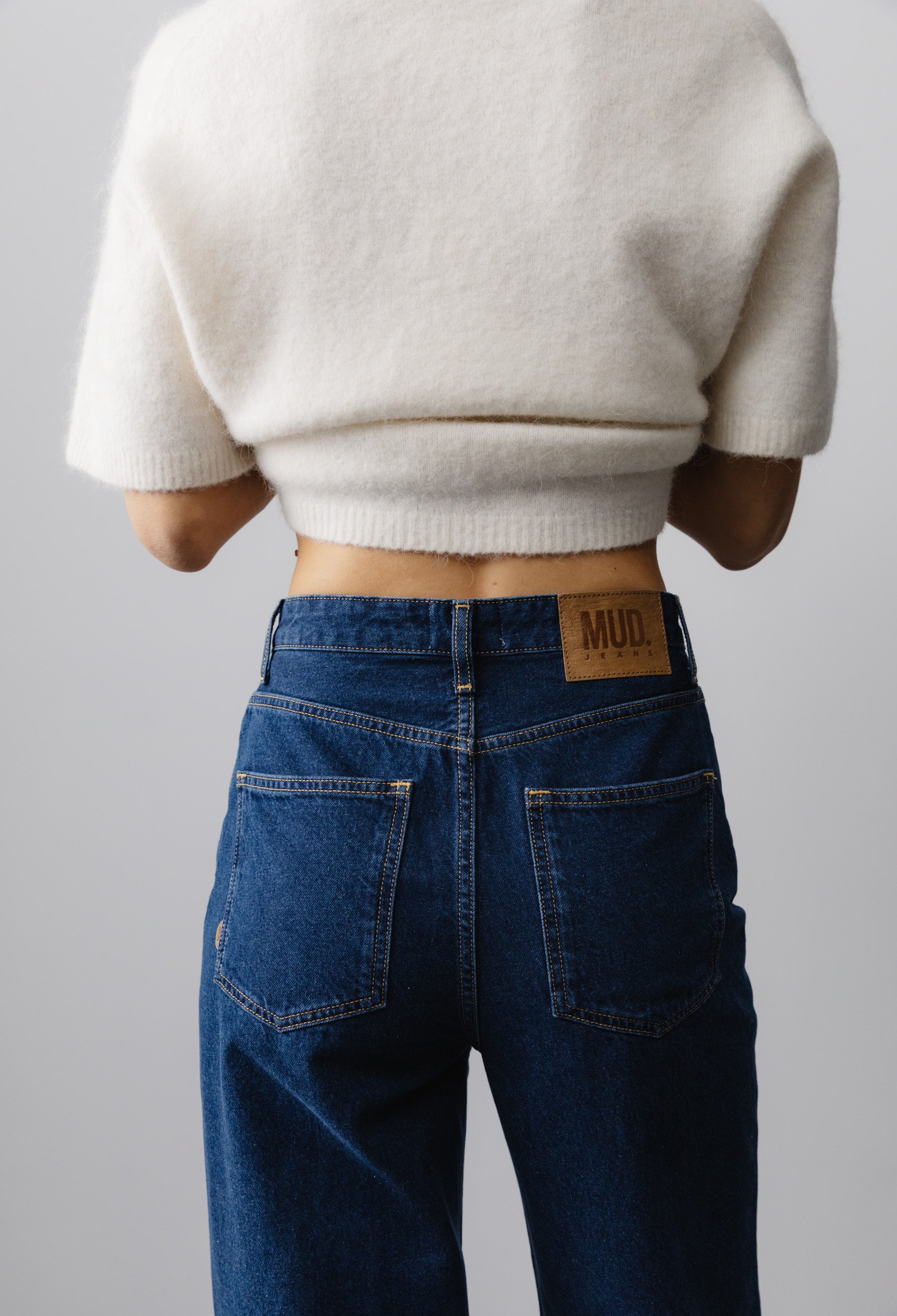 High-waisted blue MUD Jeans paired with a creamy white short-sleeve wool sweater, highlighting sustainable casual style.