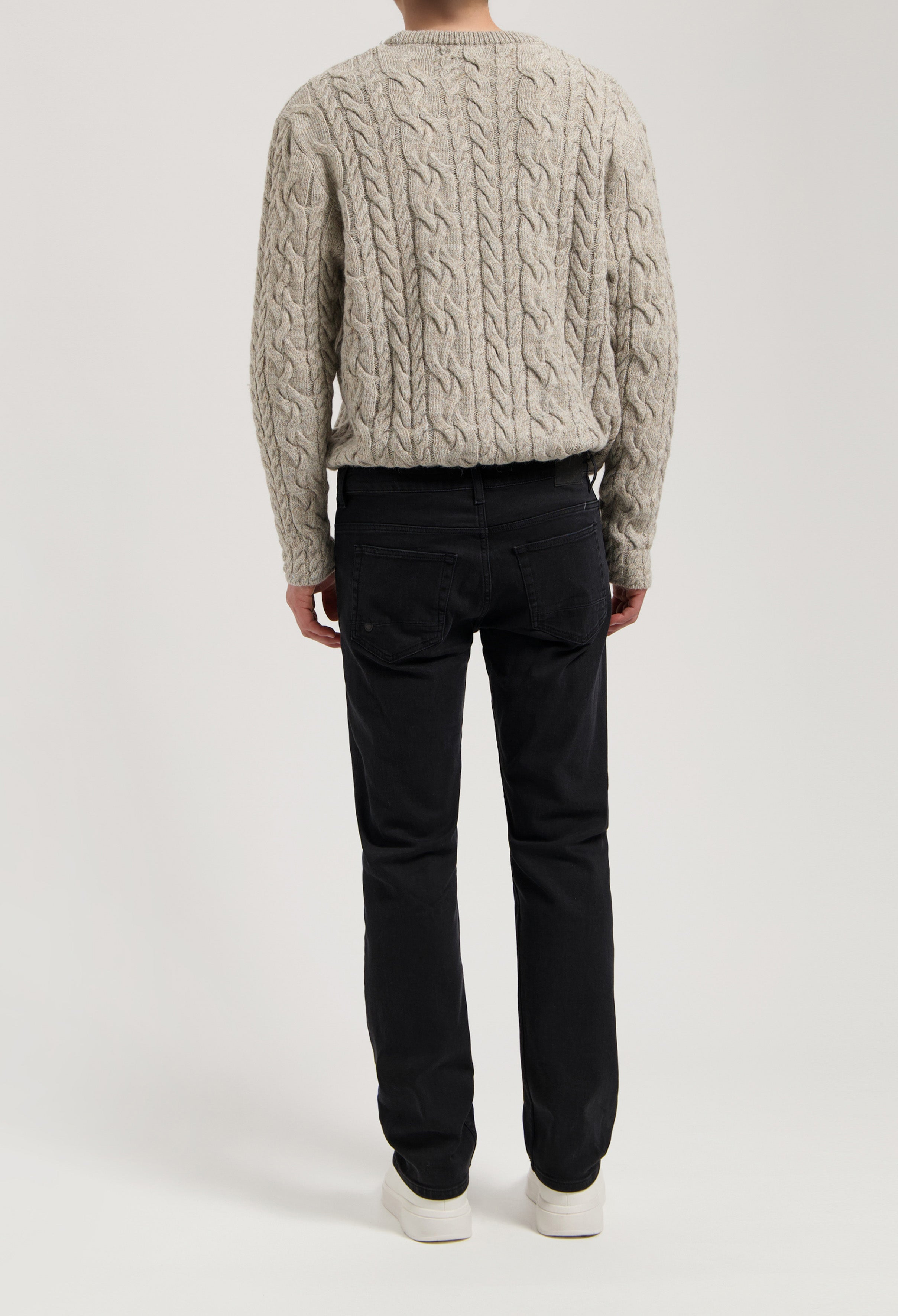 Sustainable MUD Jeans in black organic cotton, showcasing a modern fit, paired with a textured gray knitted sweater.