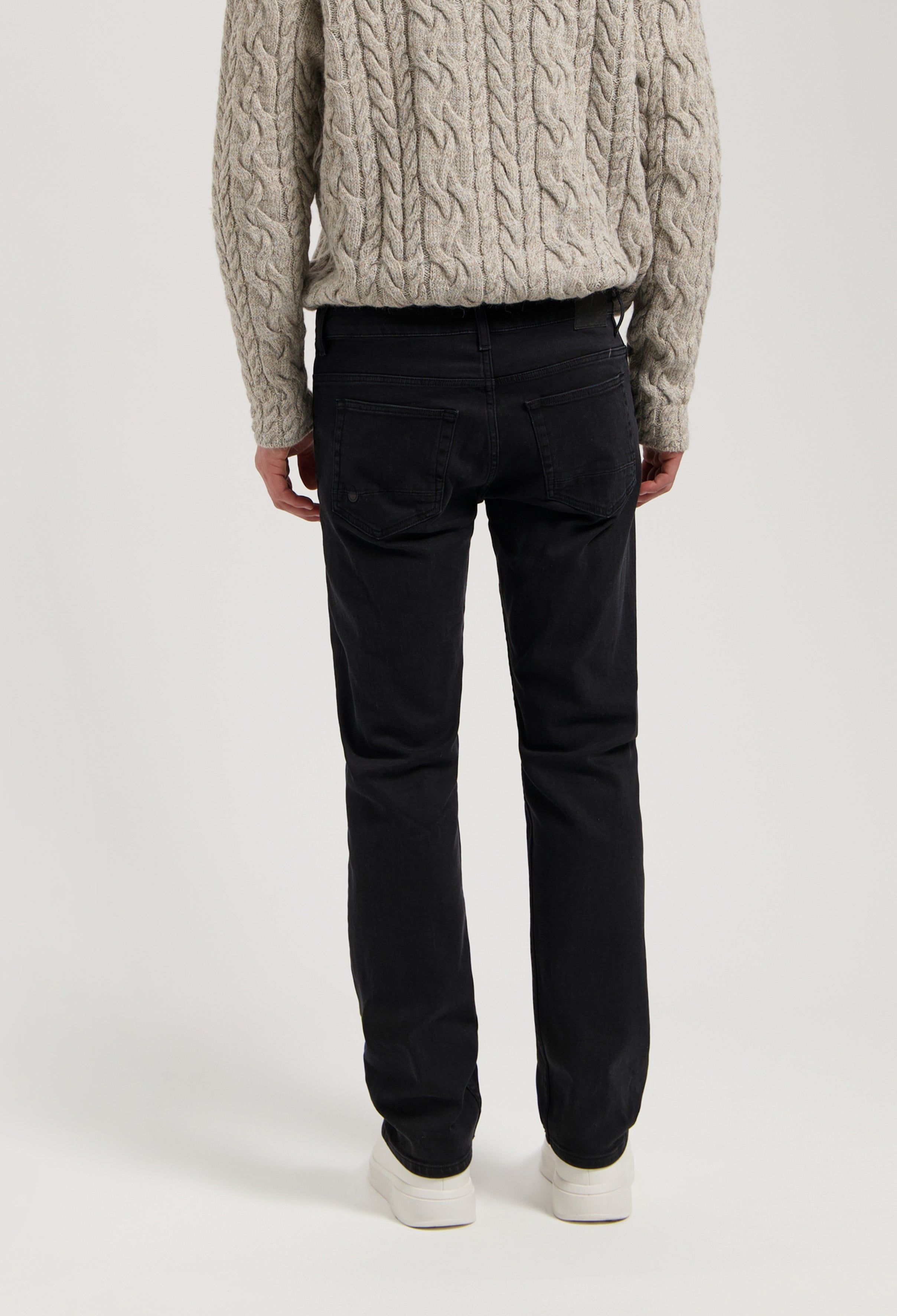 Sustainable MUD Jeans in dark denim, crafted for comfort and style, paired with a cozy gray cable-knit sweater.