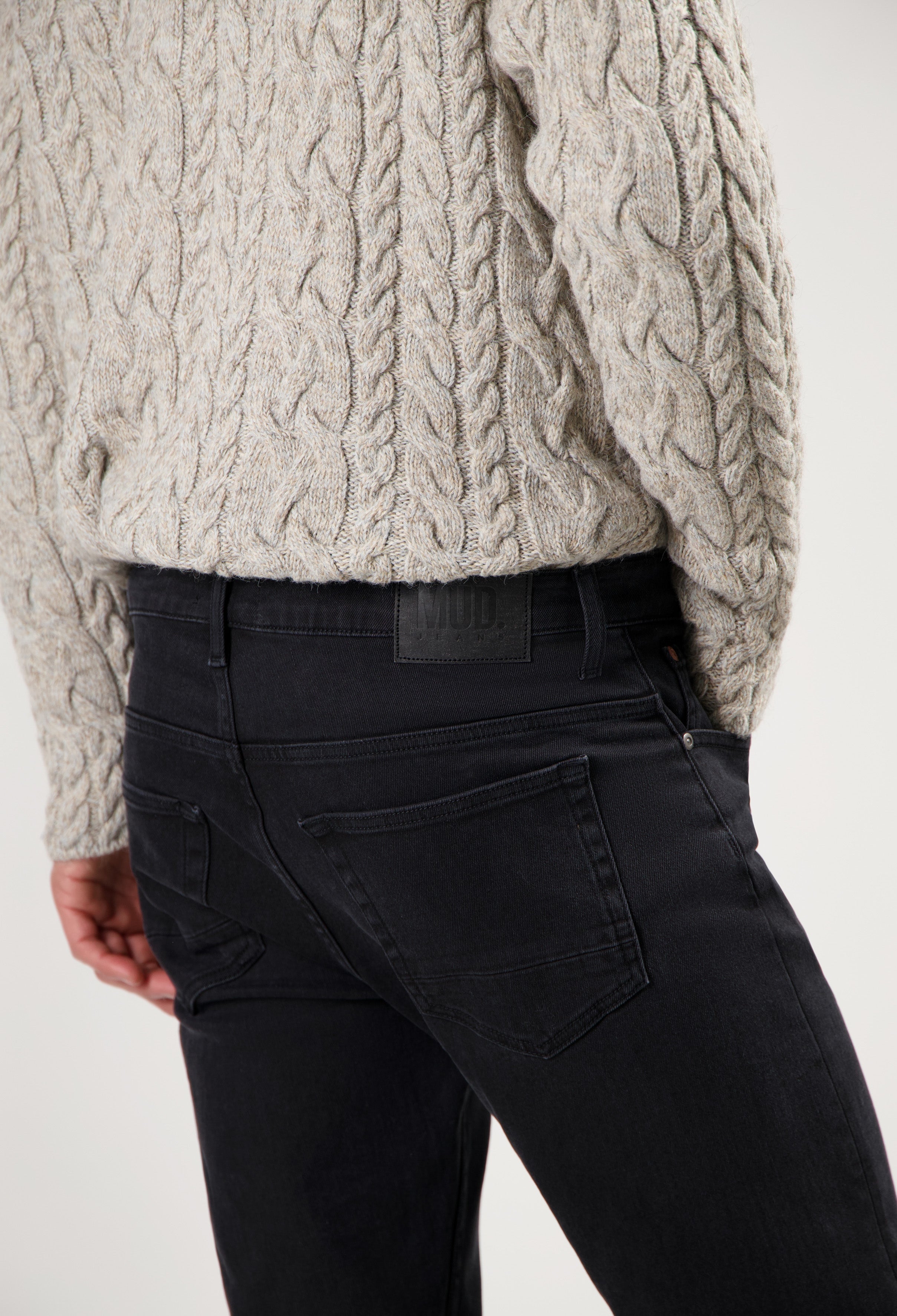 Sustainable MUD Jeans made from ethical materials, featuring dark denim, paired with a cozy beige cable-knit sweater.