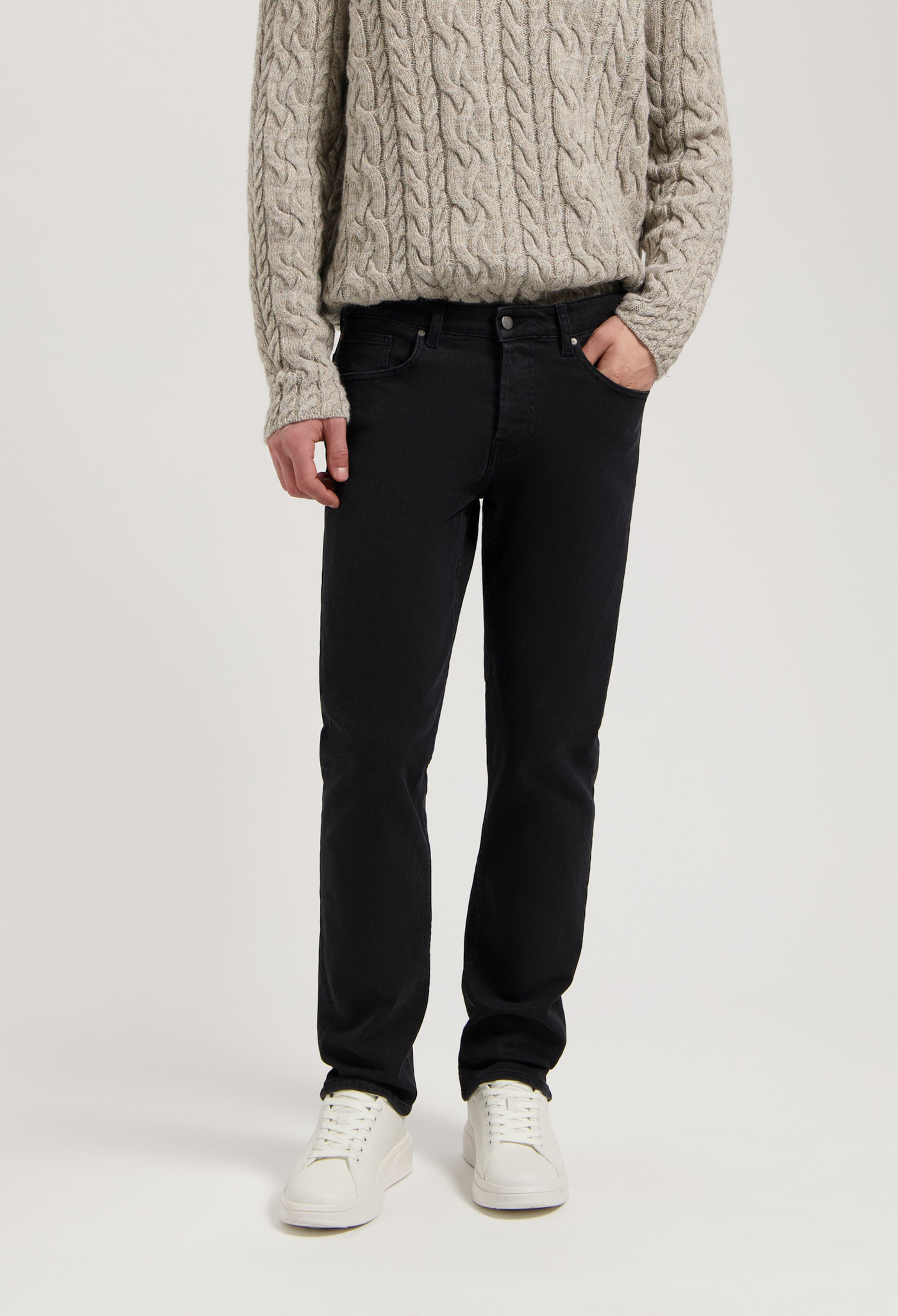 Sustainable MUD Jeans in dark denim, crafted from organic materials, paired with a textured beige sweater.