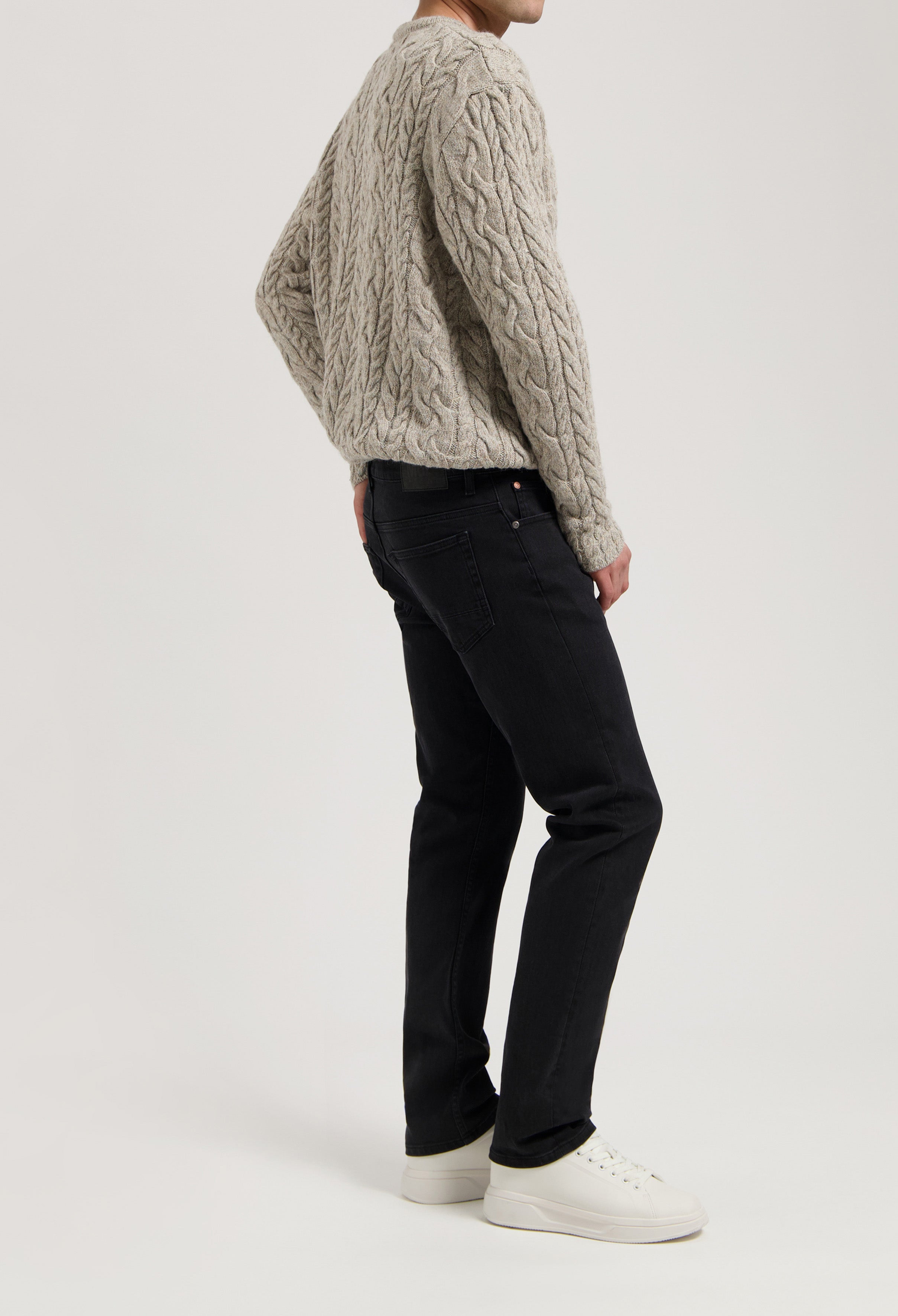 Sustainable MUD Jeans in dark denim, showcasing a classic fit, styled with an ethical beige cable-knit sweater.