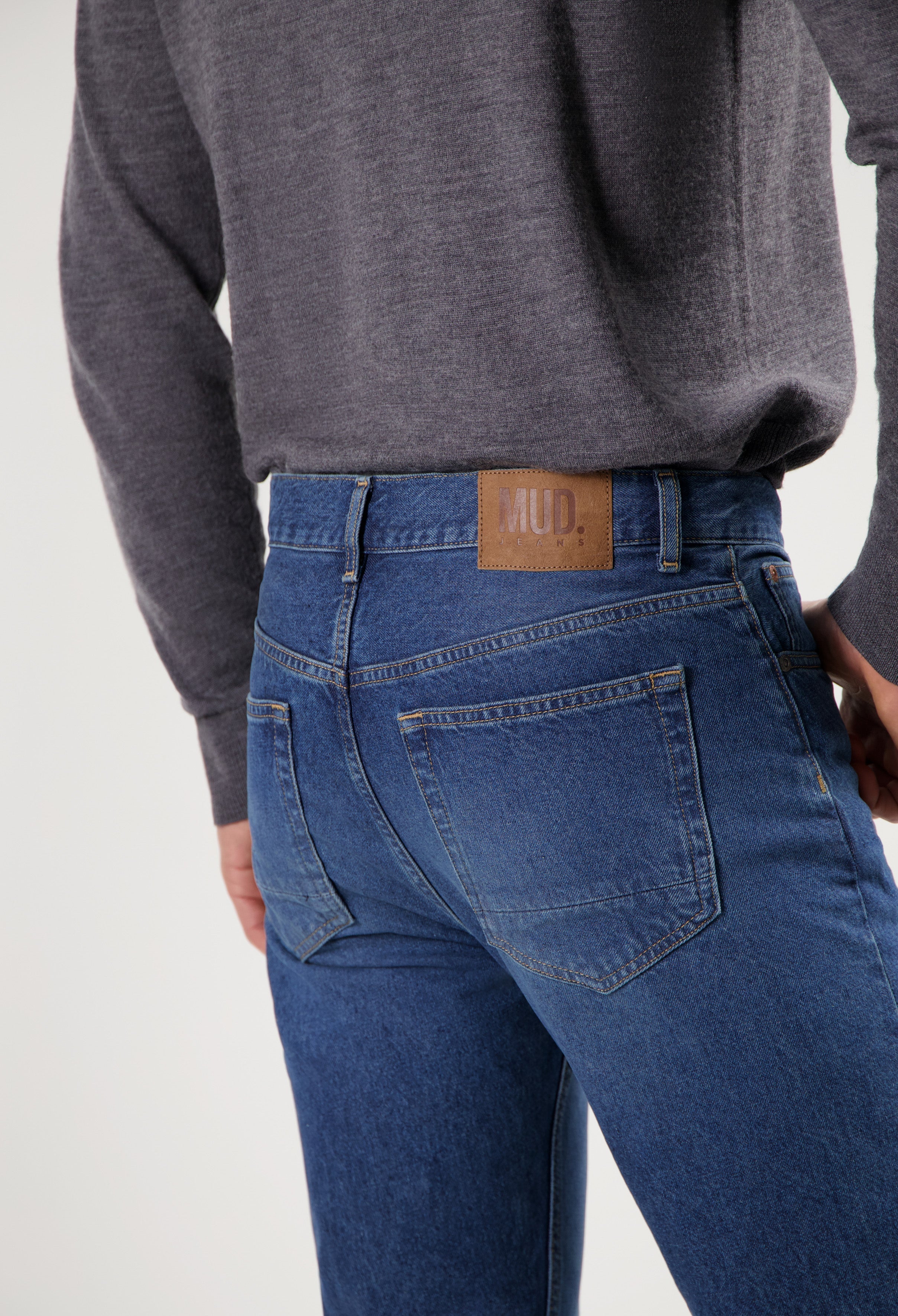 Sustainable MUD Jeans featuring classic blue denim crafted ethically, worn with a soft charcoal gray sweater.