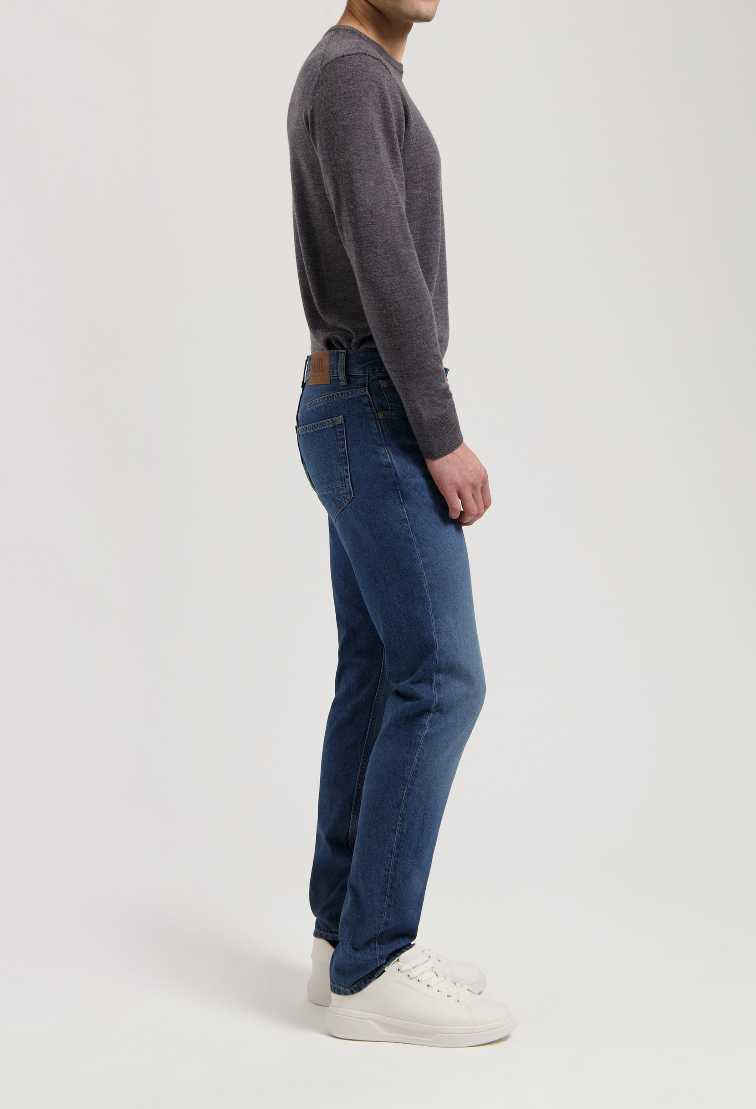 Sustainable MUD Jeans in deep blue denim, crafted ethically from organic materials, paired with a gray knit sweater.