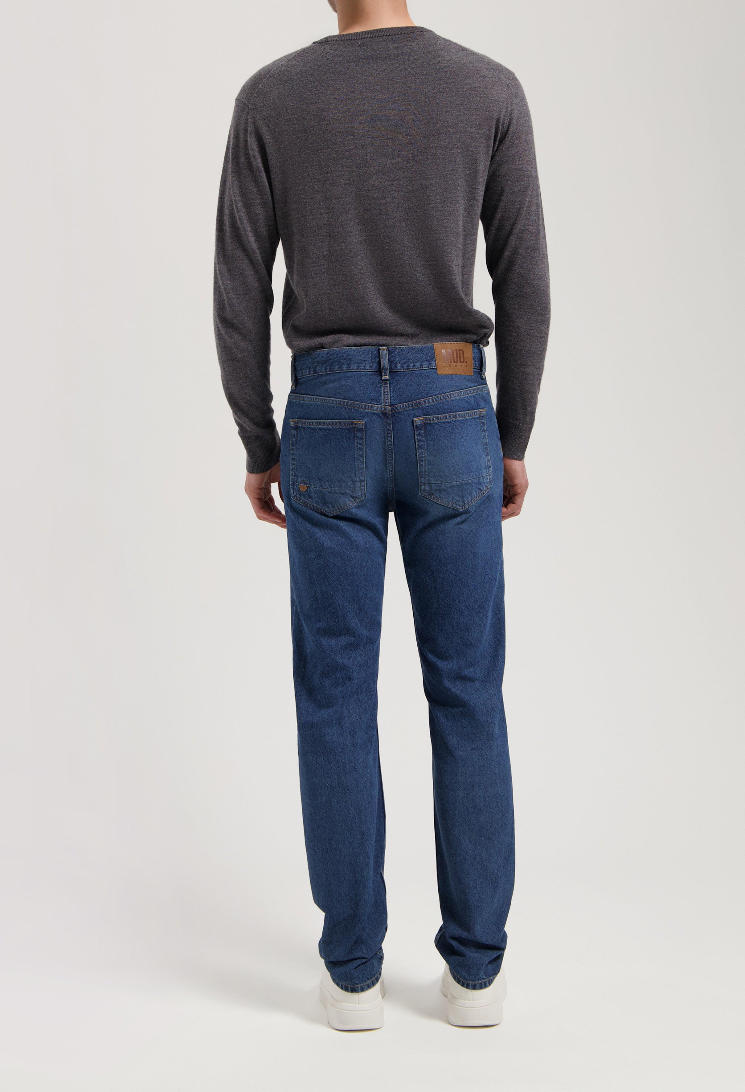 Sustainable MUD Jeans made from organic cotton in deep blue, offering a comfortable fit, paired with a dark gray sweater.