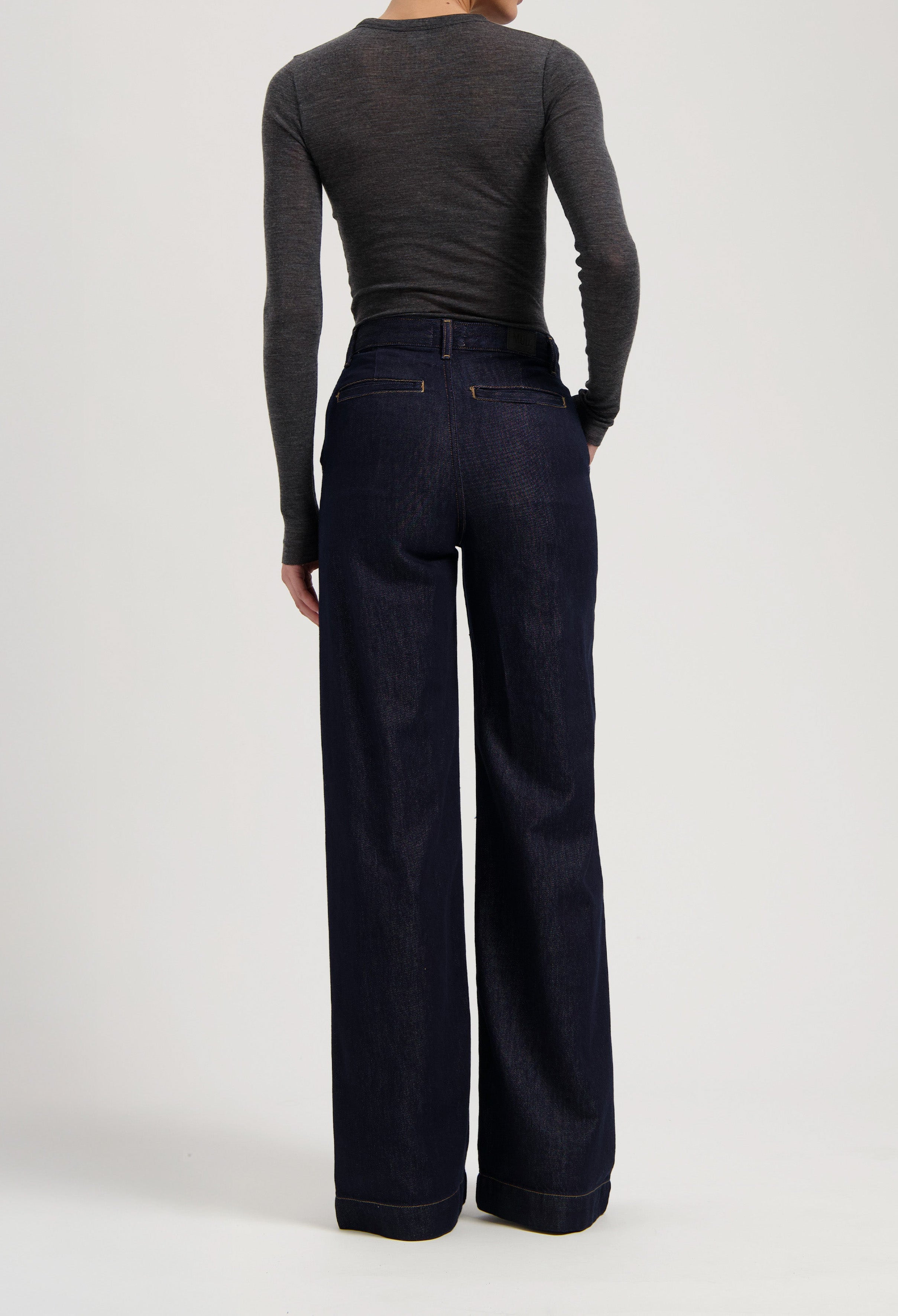 High-waisted dark blue denim jeans with wide legs, styled with a charcoal gray, long-sleeve fitted top from the back view.
