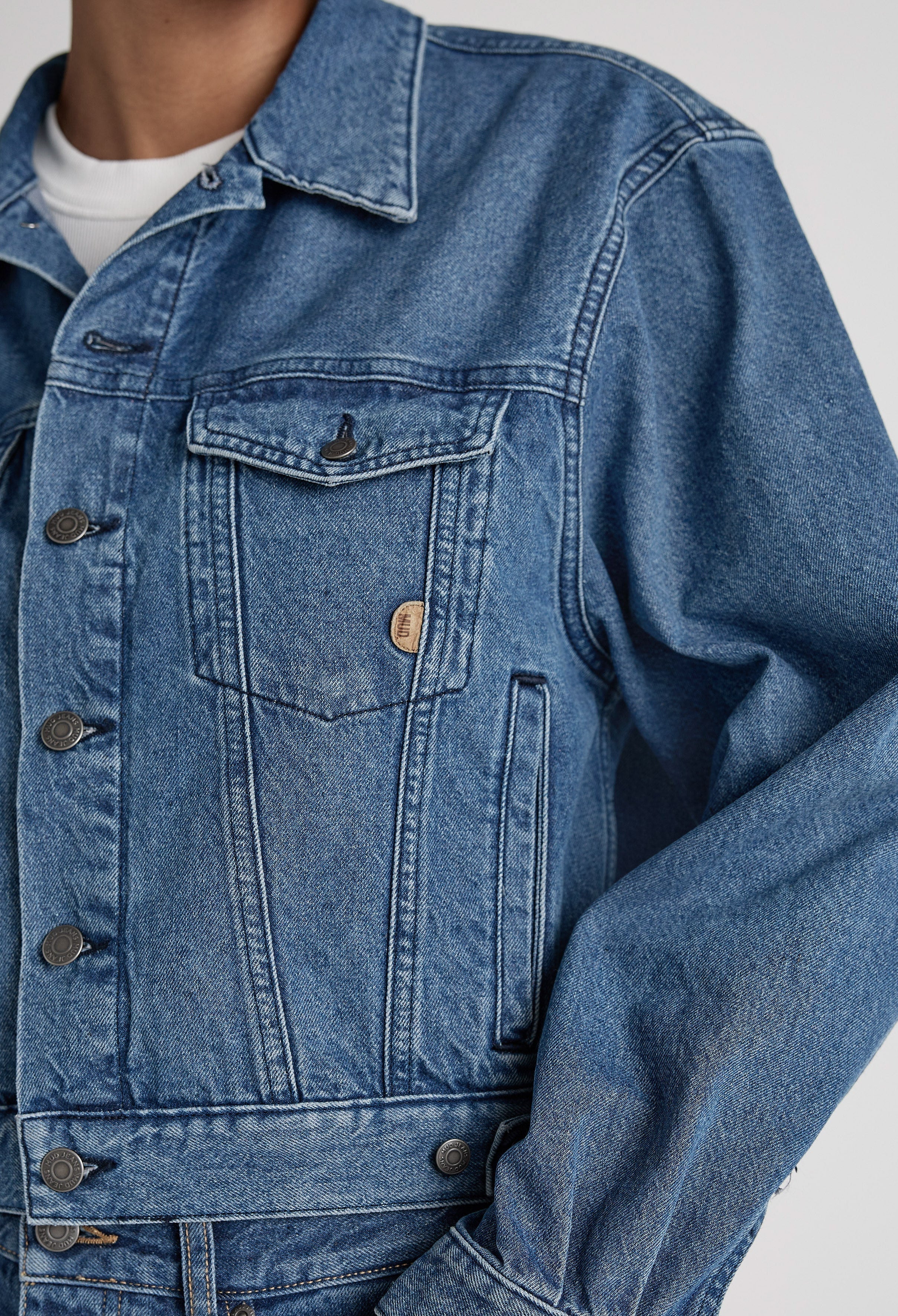 Close-up of a classic blue denim jacket with detailed stitching and metal buttons, showcasing casual style and versatility.