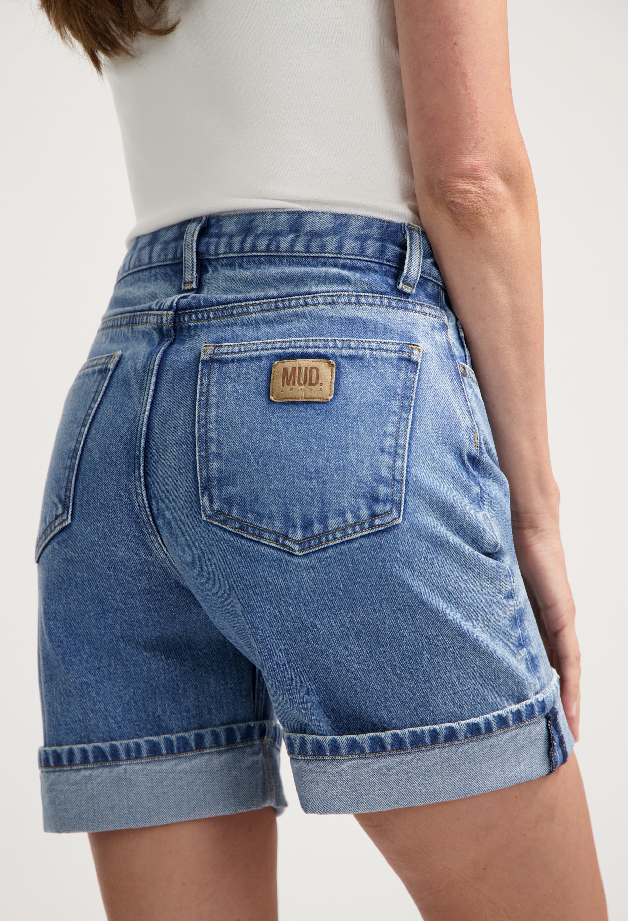 Sustainable MUD Jeans light blue denim shorts featuring rolled hems, worn with a white top for a casual summer look.