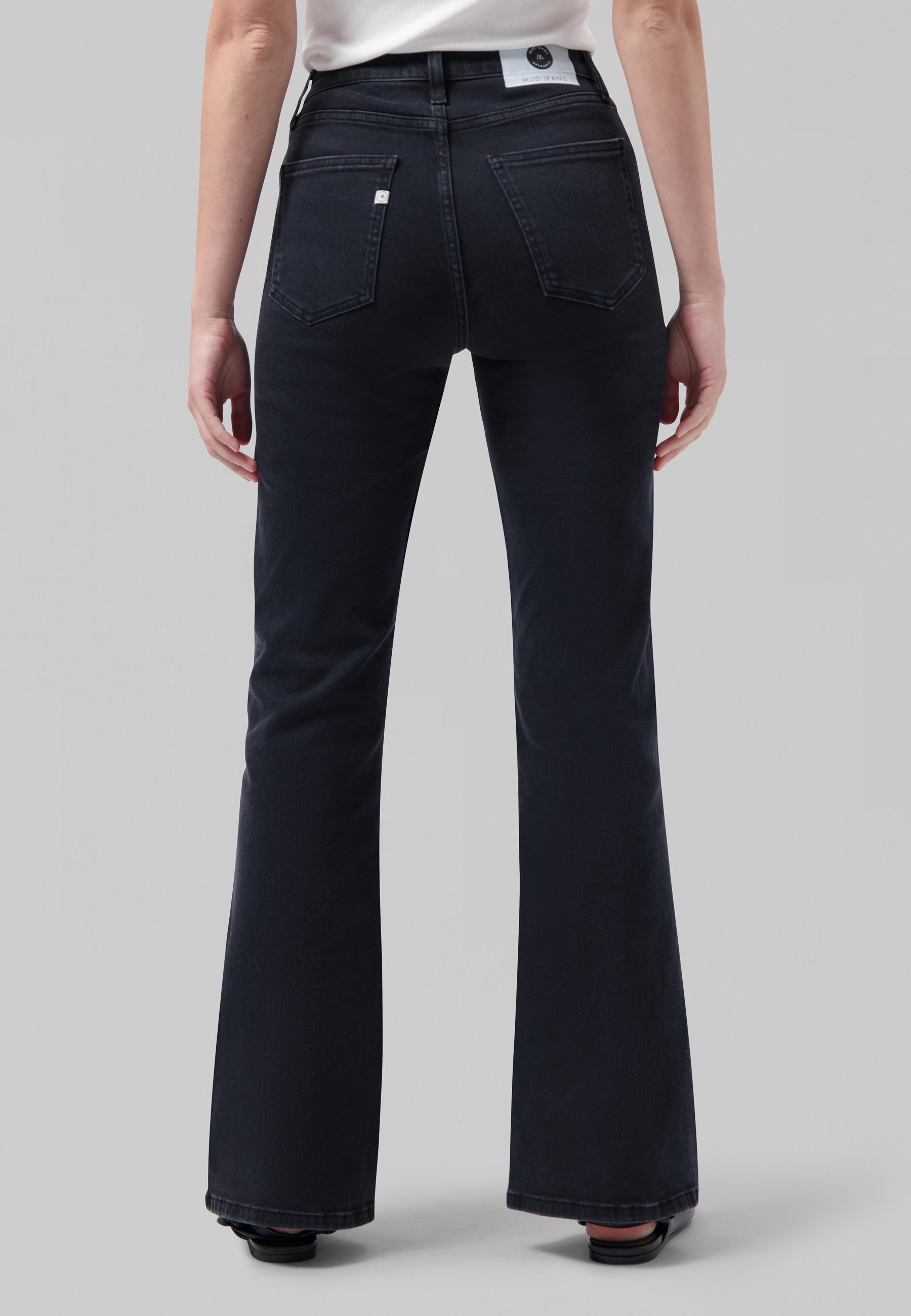 Back view of high-waisted, dark blue, flared jeans with logo patch on waistband, paired with a white top.