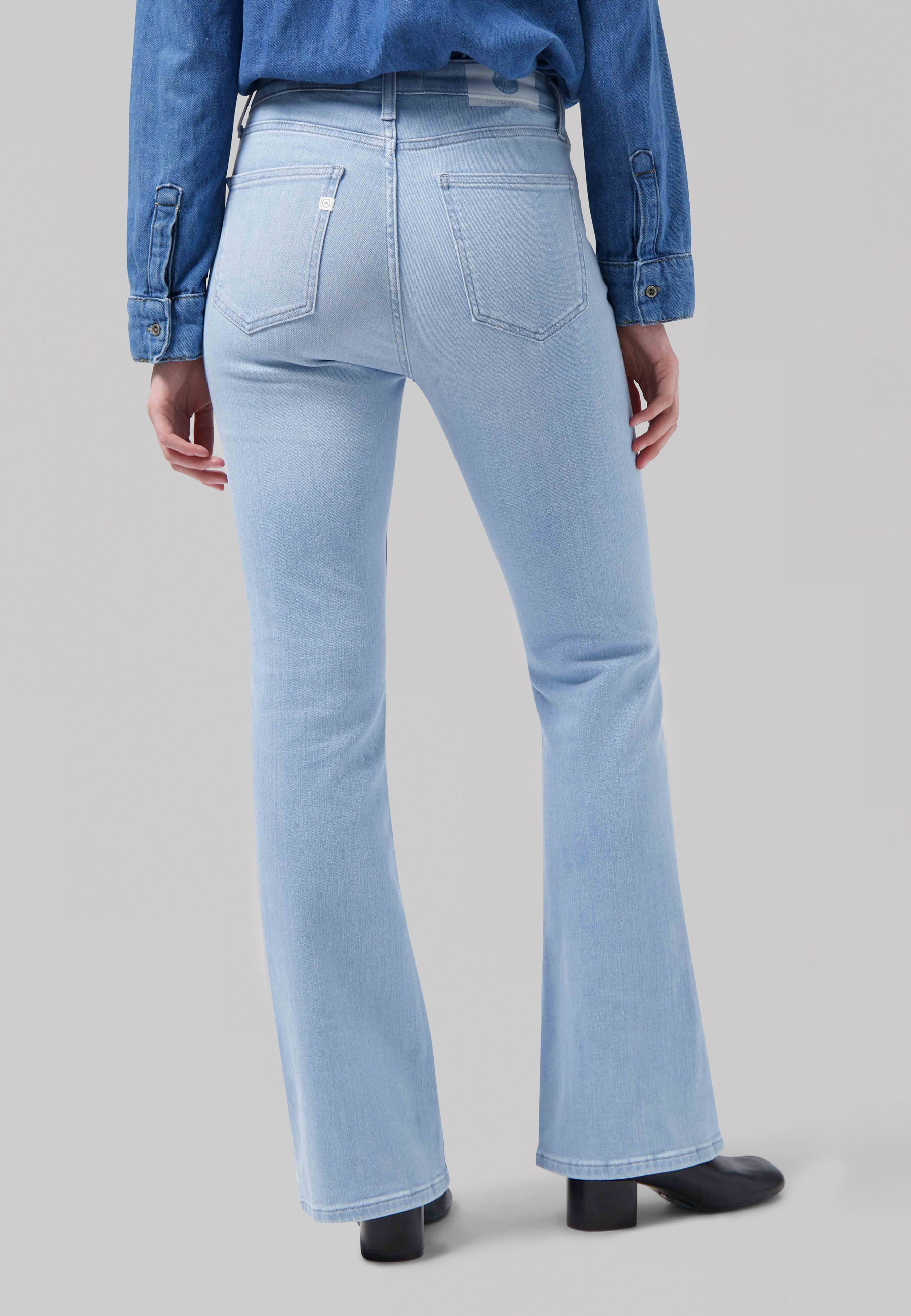 Light blue high-waisted denim jeans with a flared leg, paired with a denim shirt and black boots, showcasing a stylish back view.