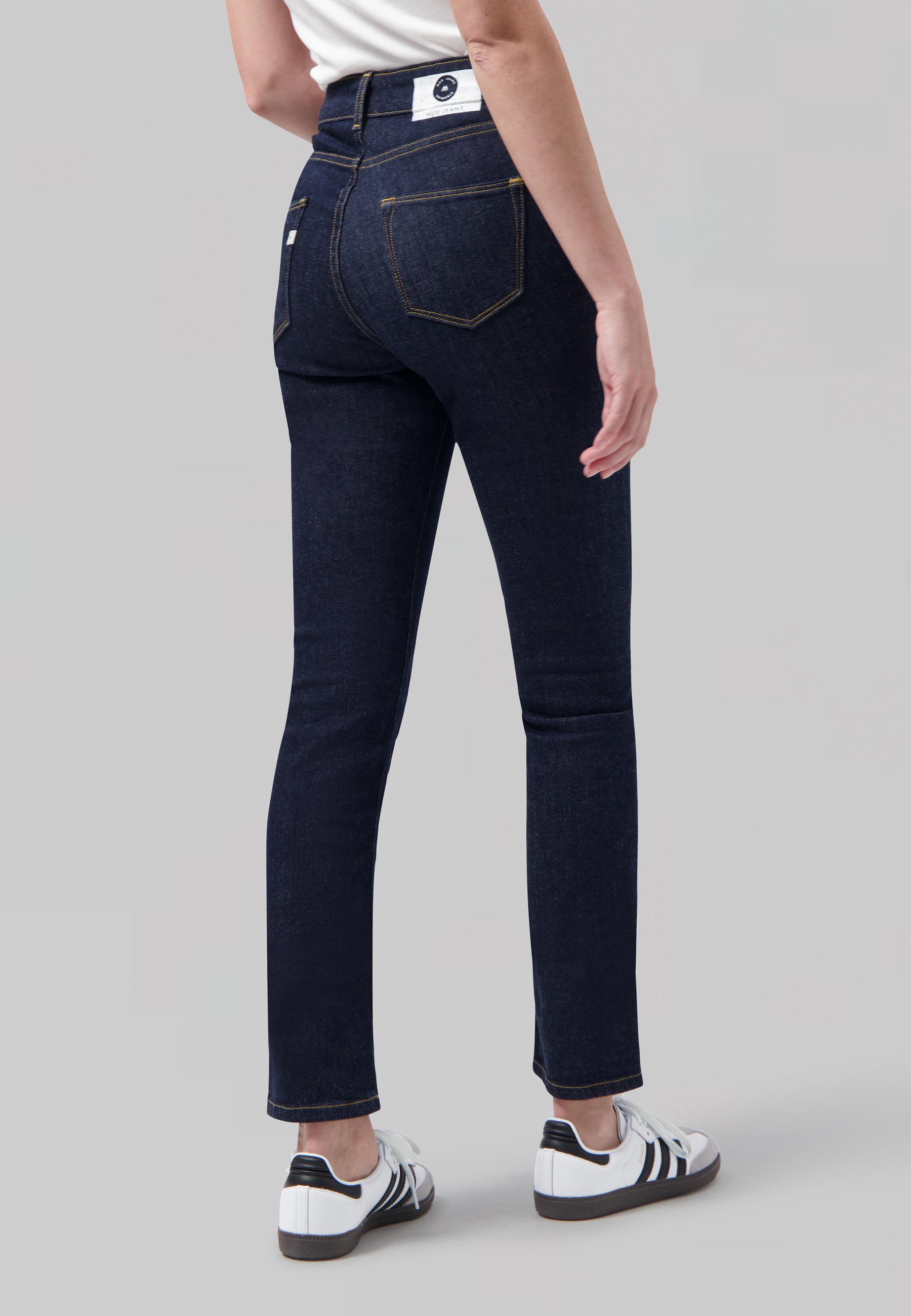 Dark blue skinny jeans with yellow stitching, back pocket detail, worn with white sneakers and a plain white top.