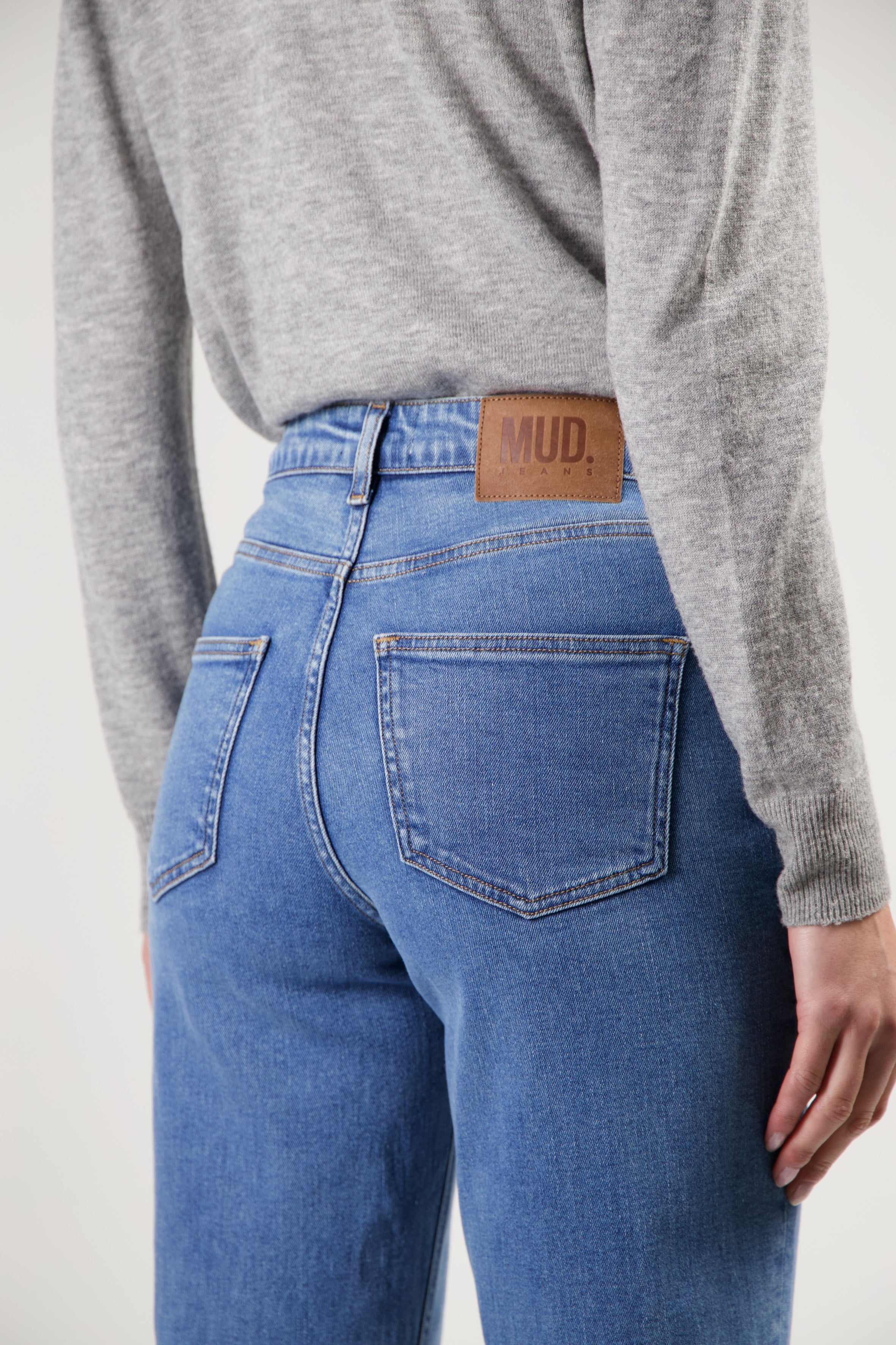 High-waisted MUD Jeans crafted from organic cotton in light blue, paired with a cozy, gray long-sleeve sweater.