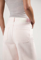 Light pink, eco-friendly MUD Jeans showcasing a high-waisted, relaxed fit, worn with a simple gray sleeveless top.