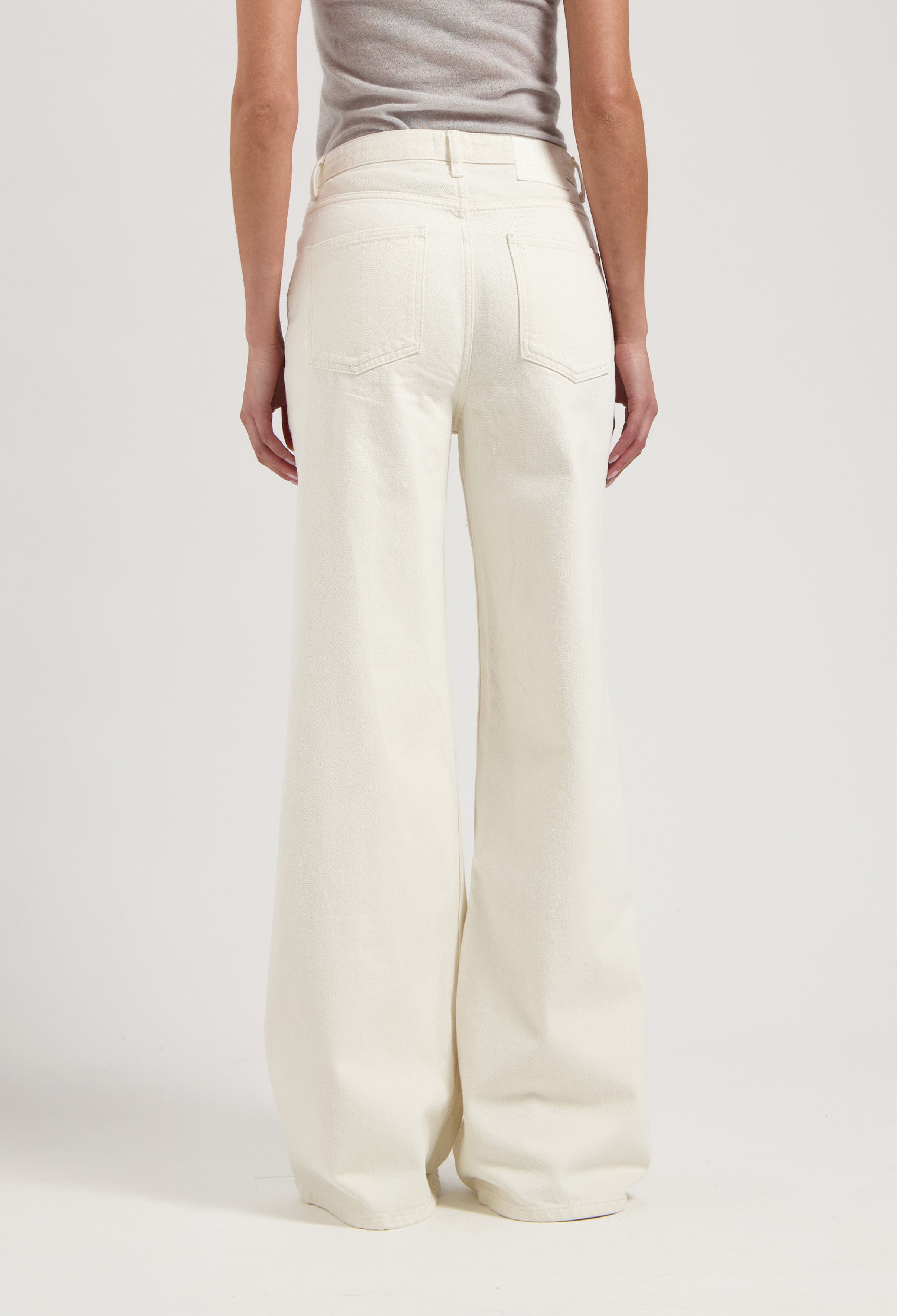 Wide-leg cream colored denim jeans showcased with a close-up back view, paired with a simple gray top.