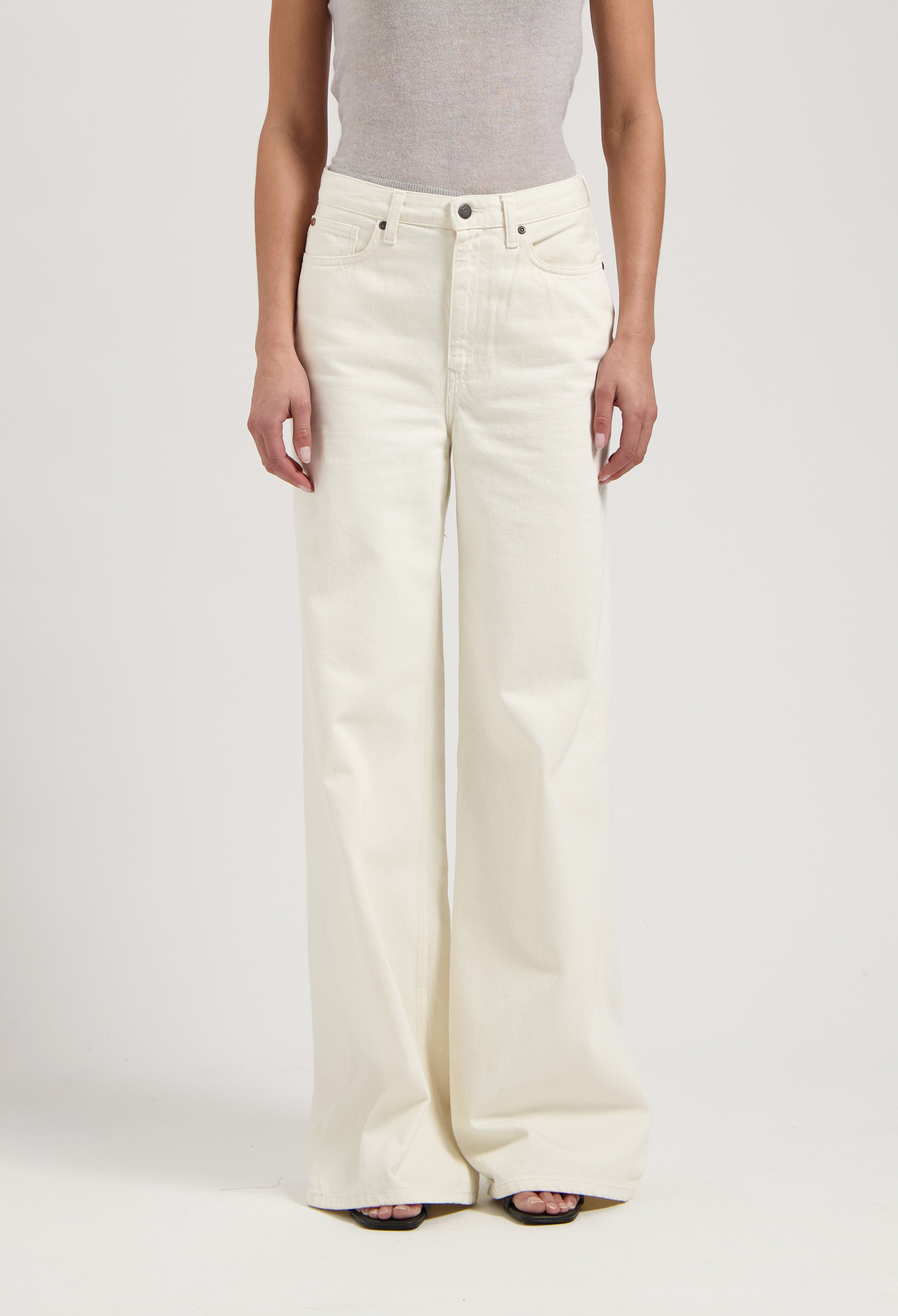 Woman wearing wide-leg, high-waisted cream jeans with a sleeveless gray top, showcasing elegant minimalist style.