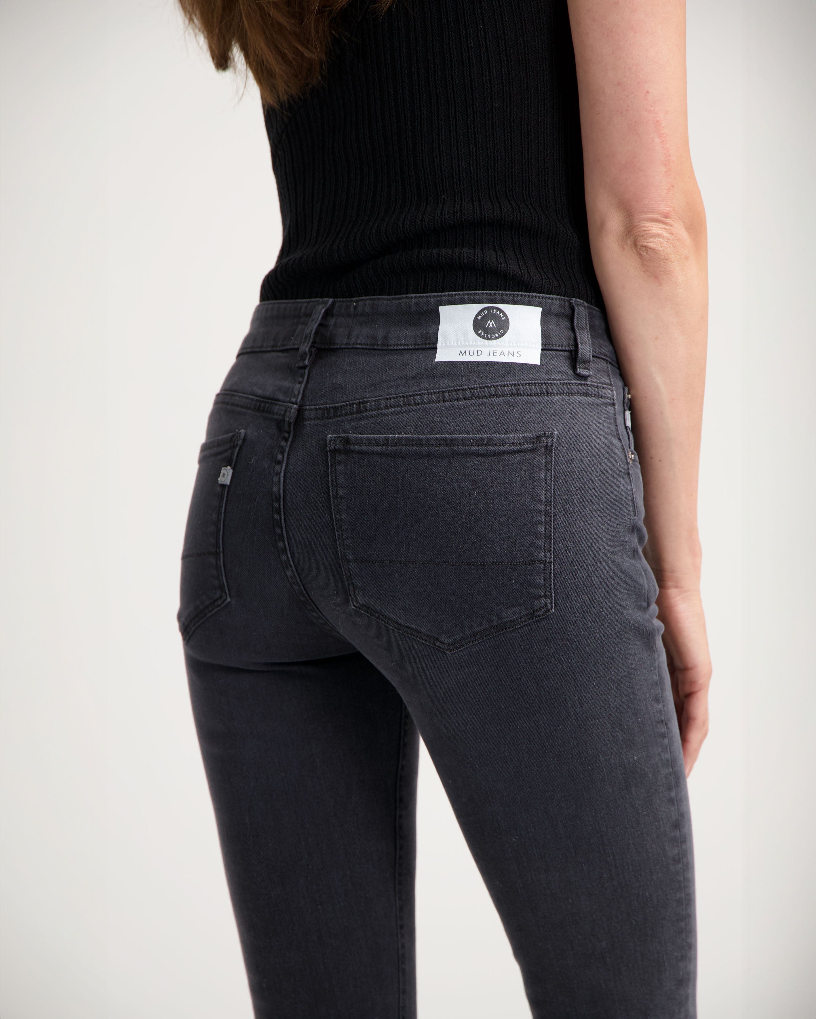 Slim-fit dark gray MUD Jeans made from organic cotton, showcasing back details with a black ribbed sleeveless top.