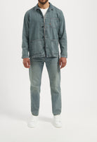 Sustainable MUD Jeans in light blue denim, ethically crafted, worn with a white T-shirt and white sneakers.